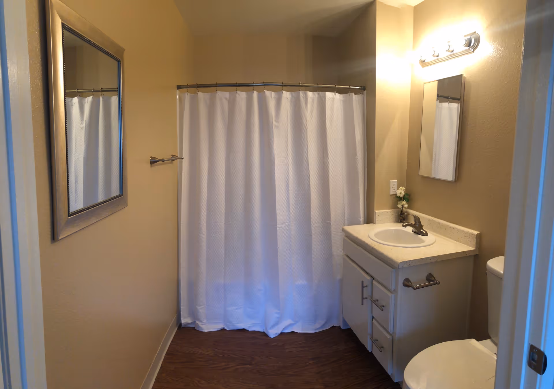 Small bathroom with sink, mirror, toilet, and white shower curtain in warm beige walls.