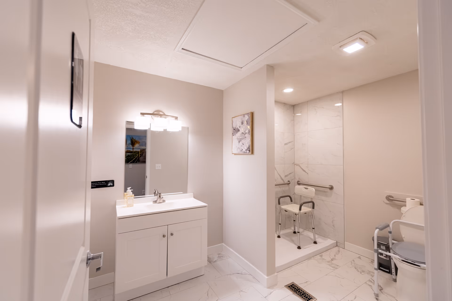 Accessible bathroom with sink, mirror, marble-tiled shower area, and grab bars.