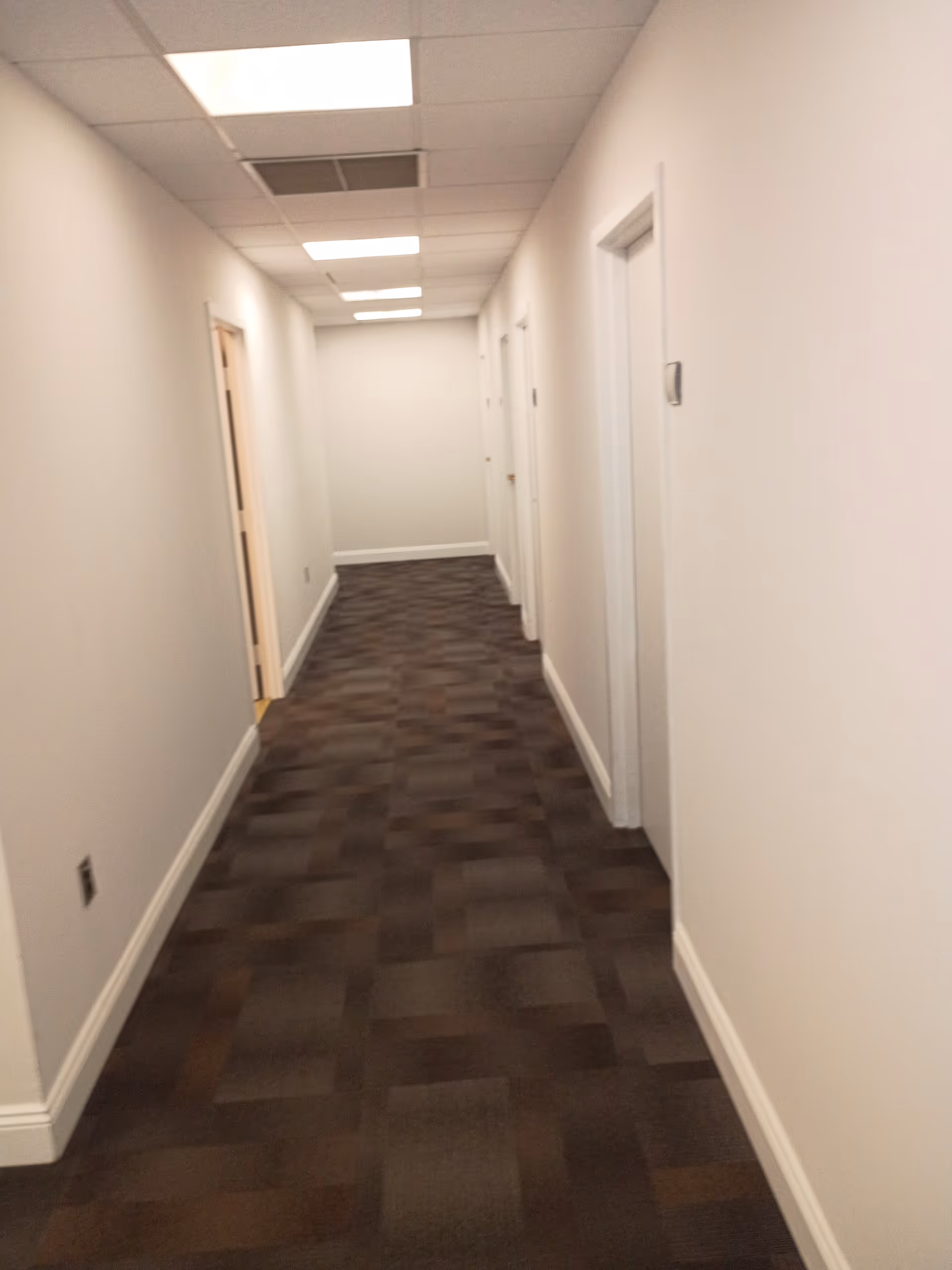 A narrow, well-lit hallway inside a senior living facility with white walls and brown carpet.