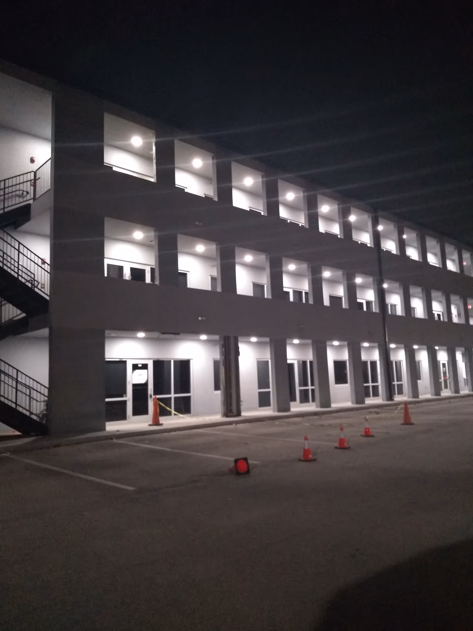 Night exterior of a multi-story senior living building with illuminated entrances and a parking lot.