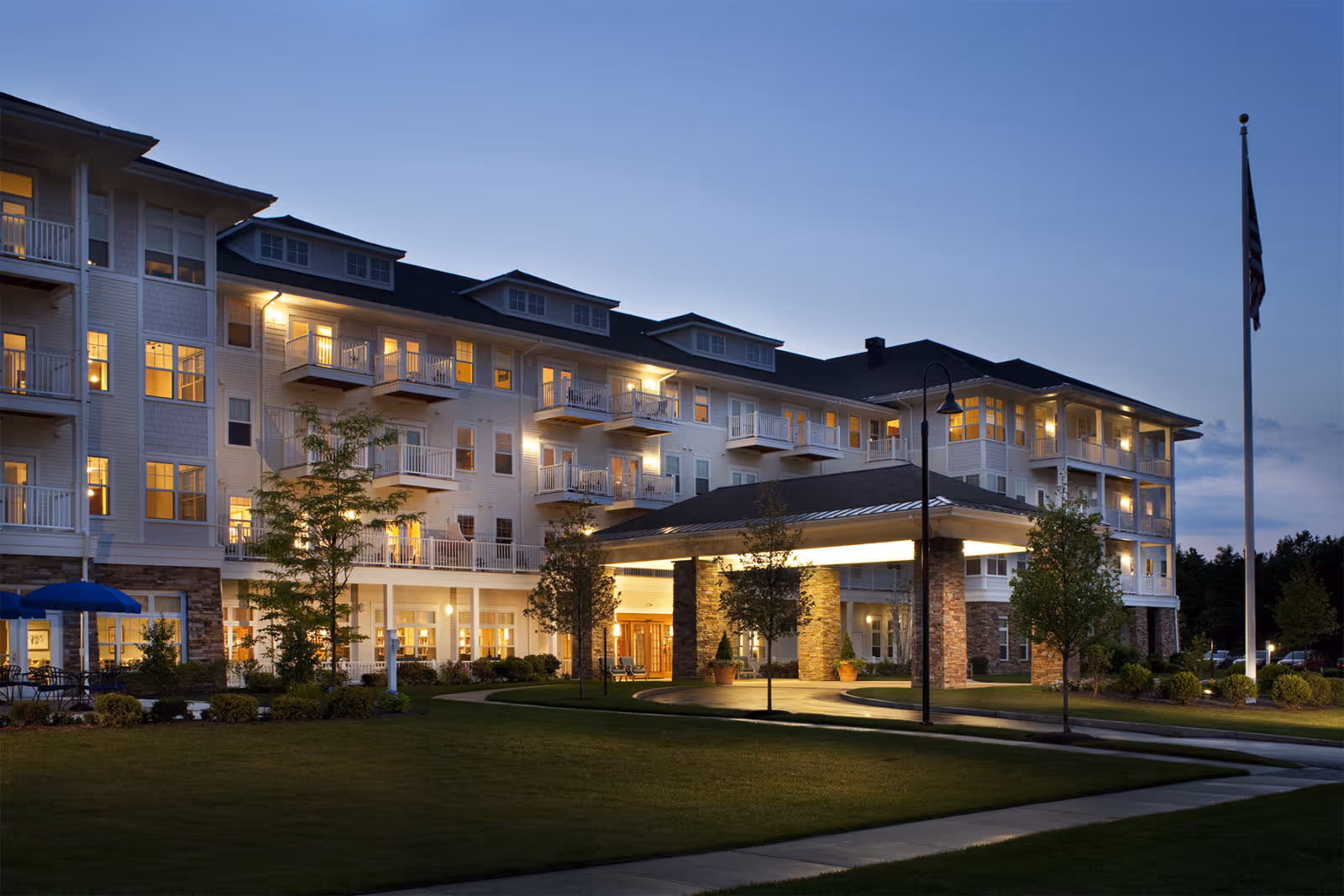 Exterior view of a multi-story senior living facility with illuminated entrance at dusk