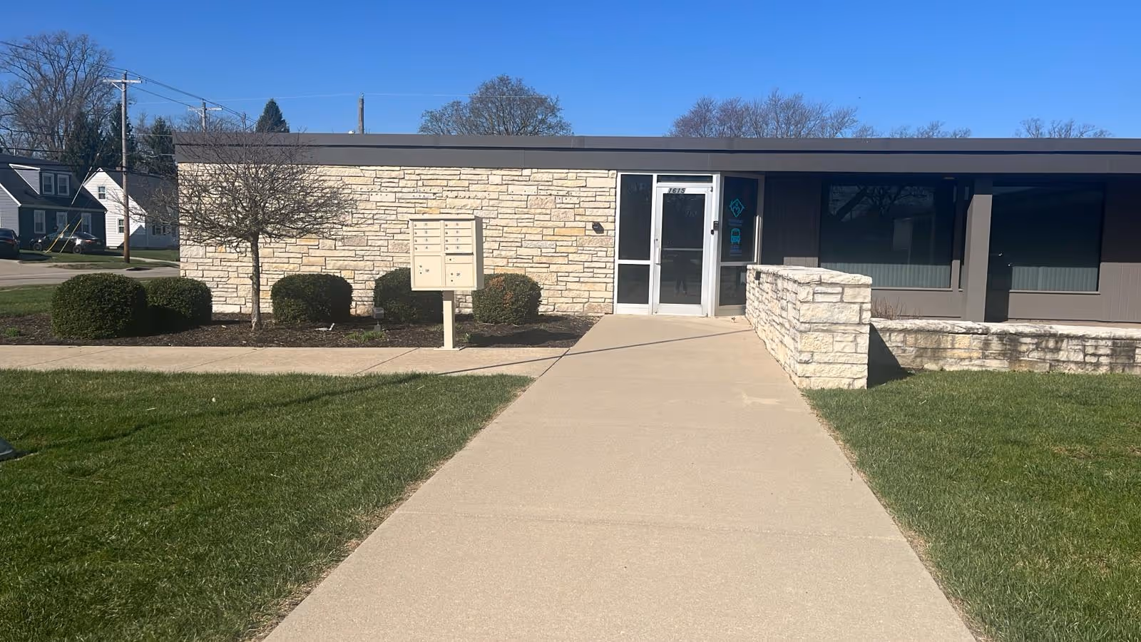 A single-story senior living facility with a glass door entrance, walkway, and manicured landscaping.
