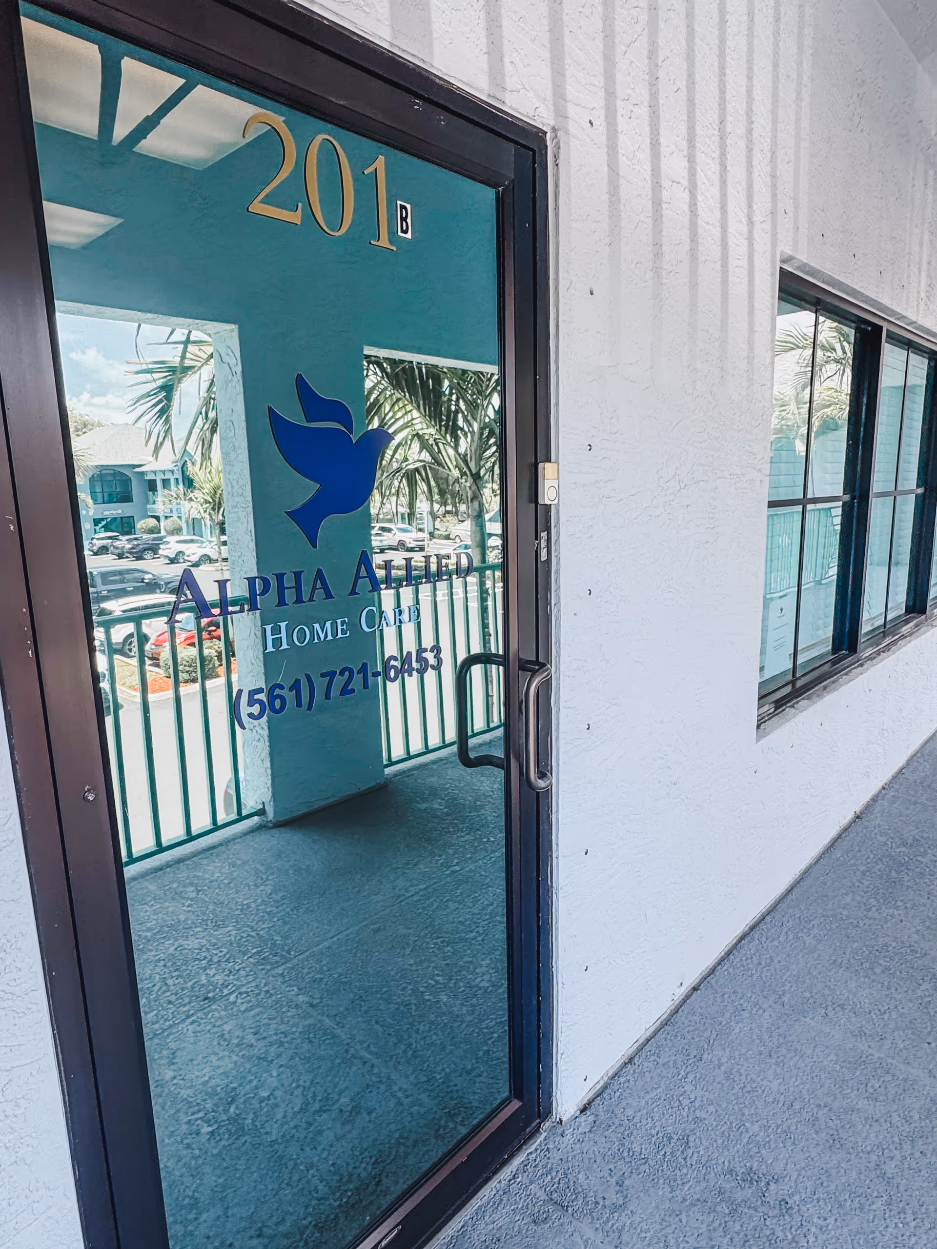 A glass door displays Alpha Allied Home Care sign, entrance to facility, unit 201B.