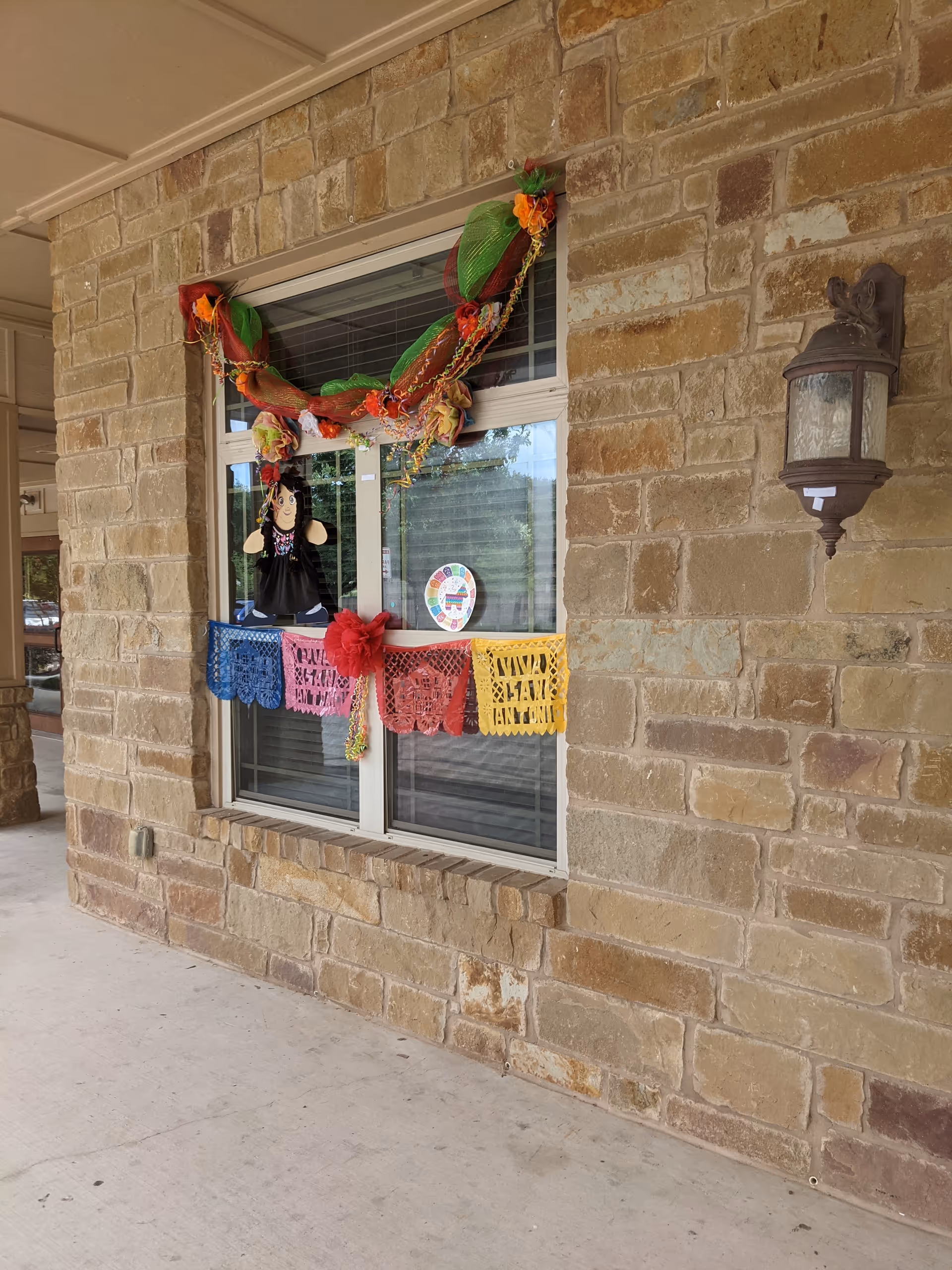 Stone exterior wall with a window decorated by colorful garlands and a lantern.