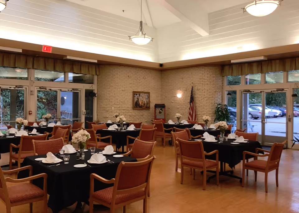 Spacious dining room with round tables, black tablecloths, and floral centerpieces.