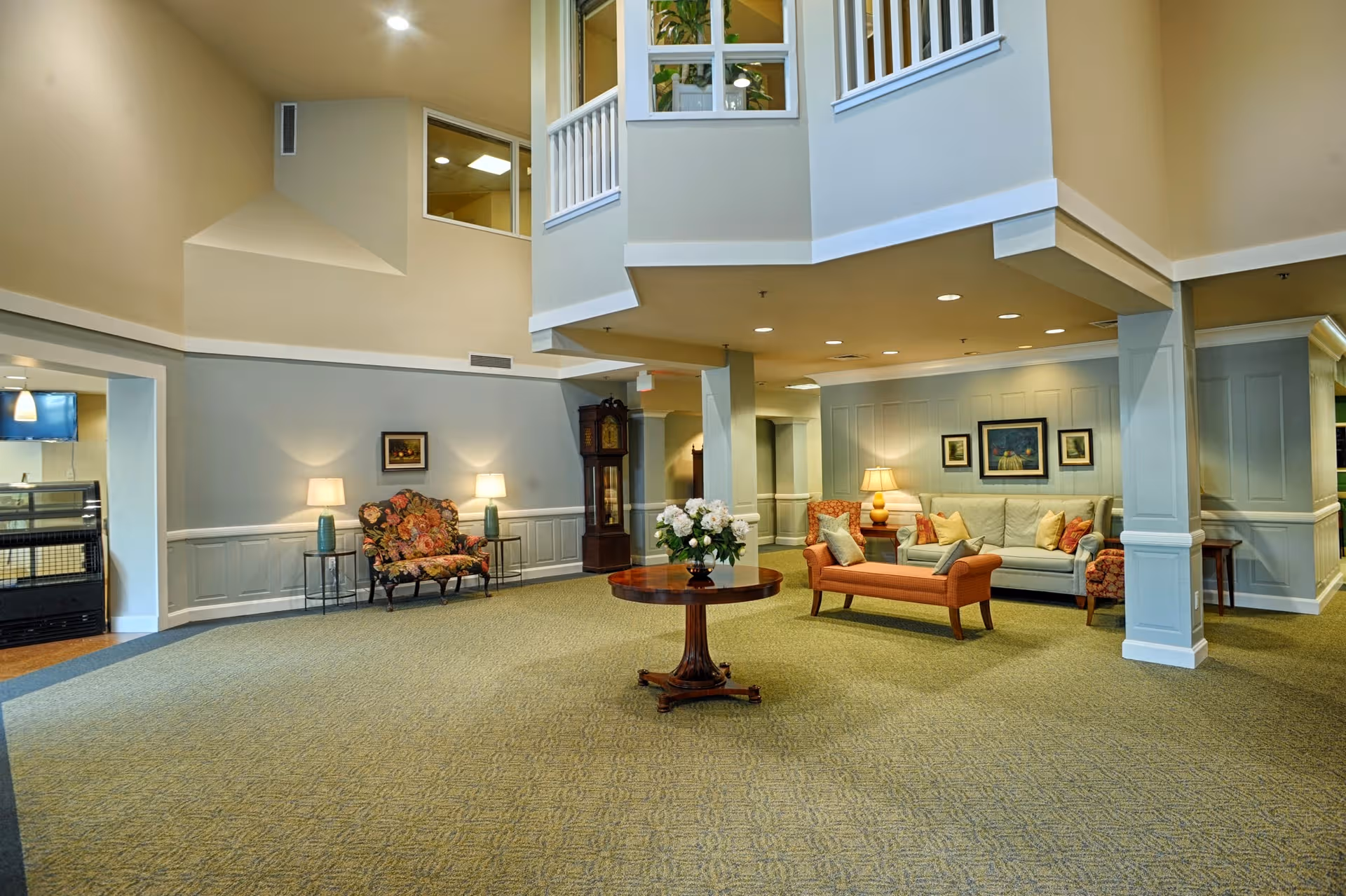 Spacious senior living facility lobby with sofas, chairs, lamps, and a central round table.