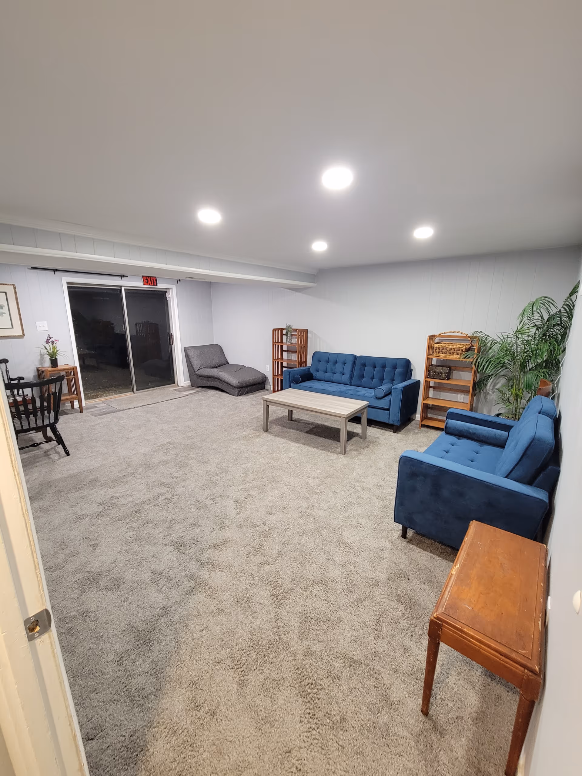 Cozy senior living common area with blue sofas, a coffee table, and a doorway to outside.