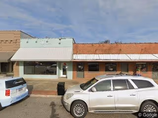 Exterior view of a strip storefront with parked cars in front.