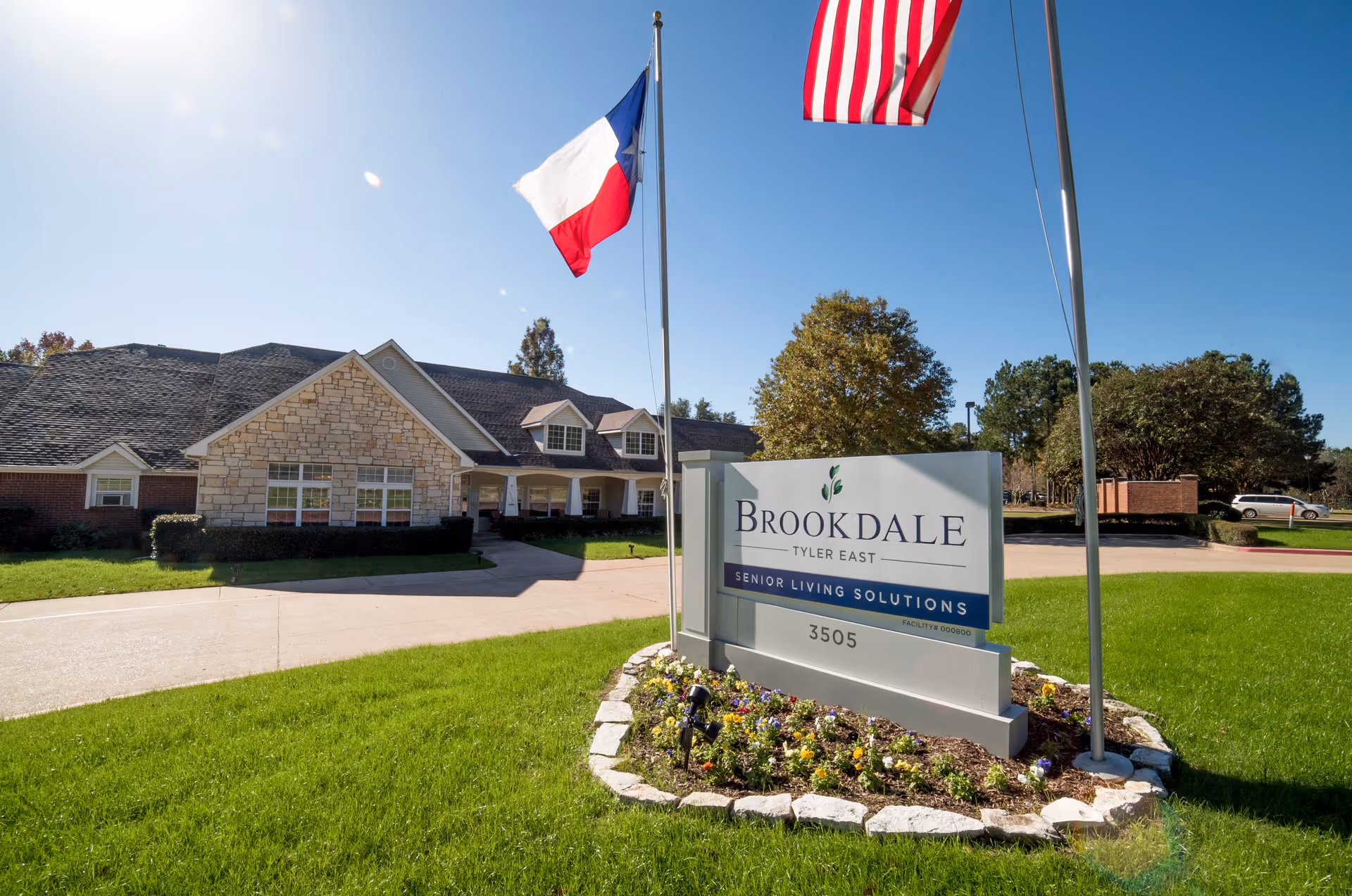 Exterior view of Brookdale Tyler East senior living facility with sign and flags.