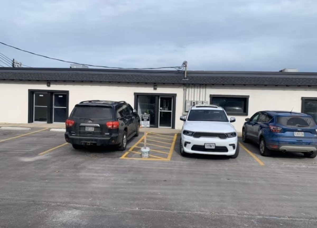 A parking lot in front of a single-story building, three cars parked by the entrance.