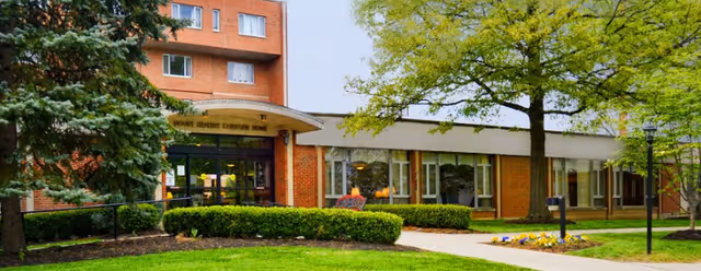 Brick senior living facility exterior with glass entrance doors and landscaped surroundings.