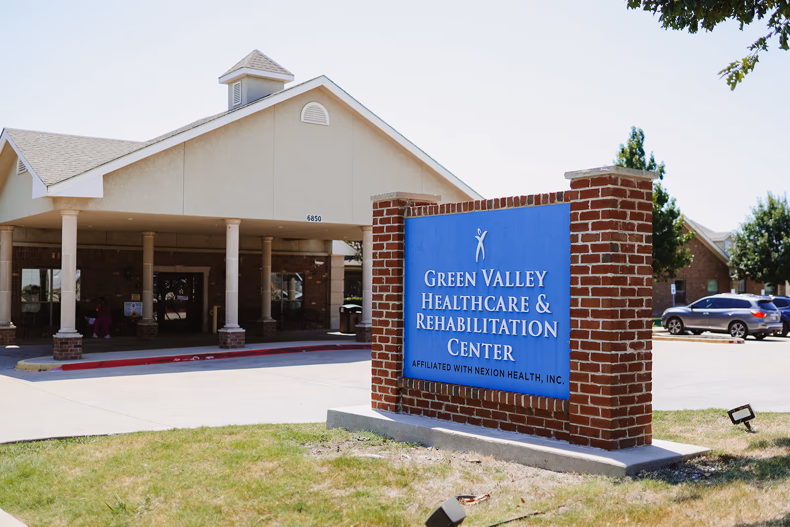 Exterior view of Green Valley Healthcare and Rehabilitation Center with blue sign near entrance