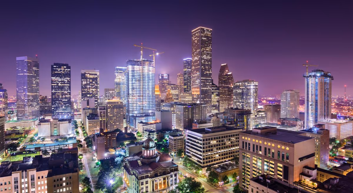 Nighttime aerial cityscape with illuminated skyscrapers and glowing streets.