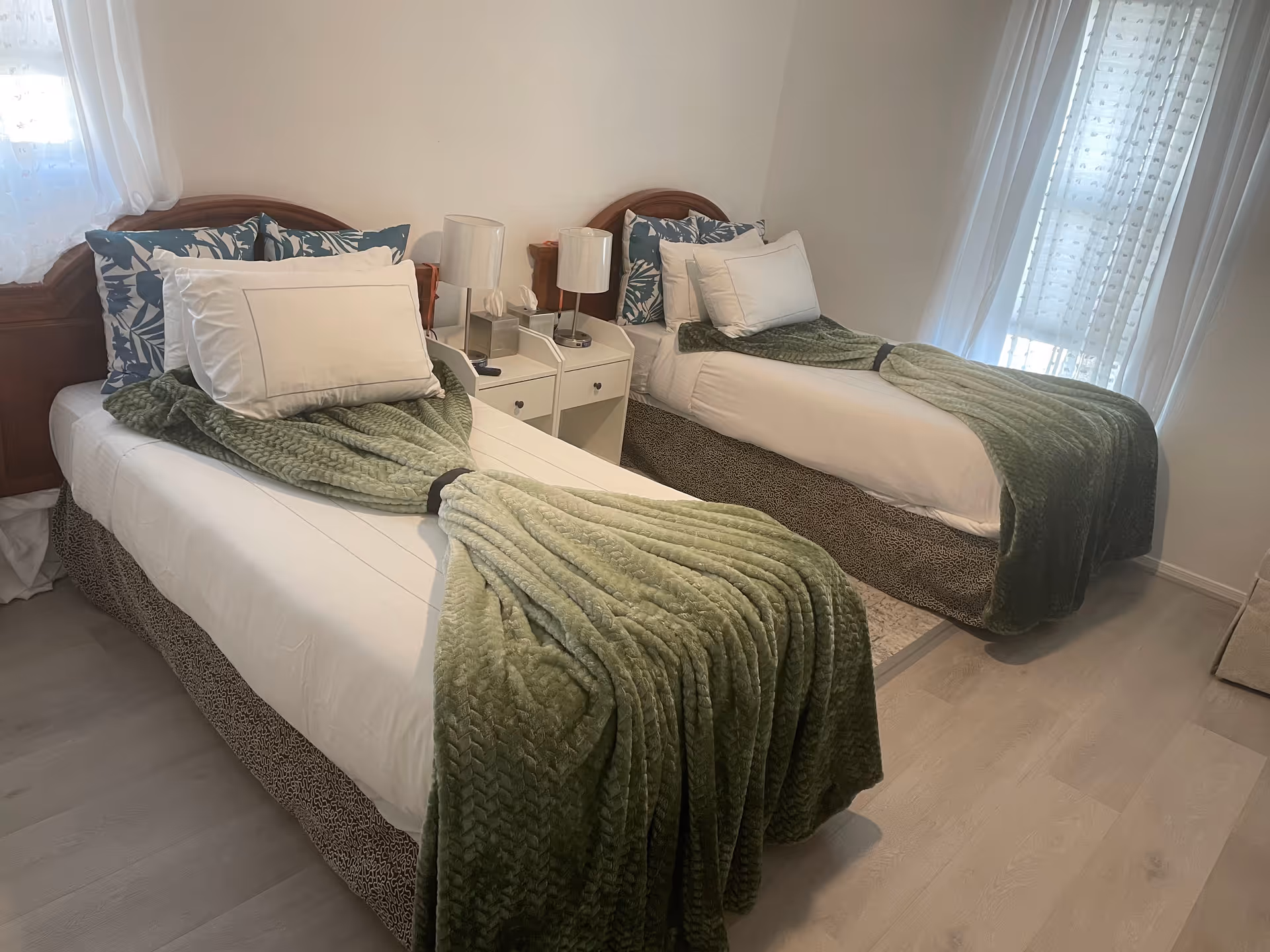 Two twin beds with green throws and lamps in a bright bedroom.