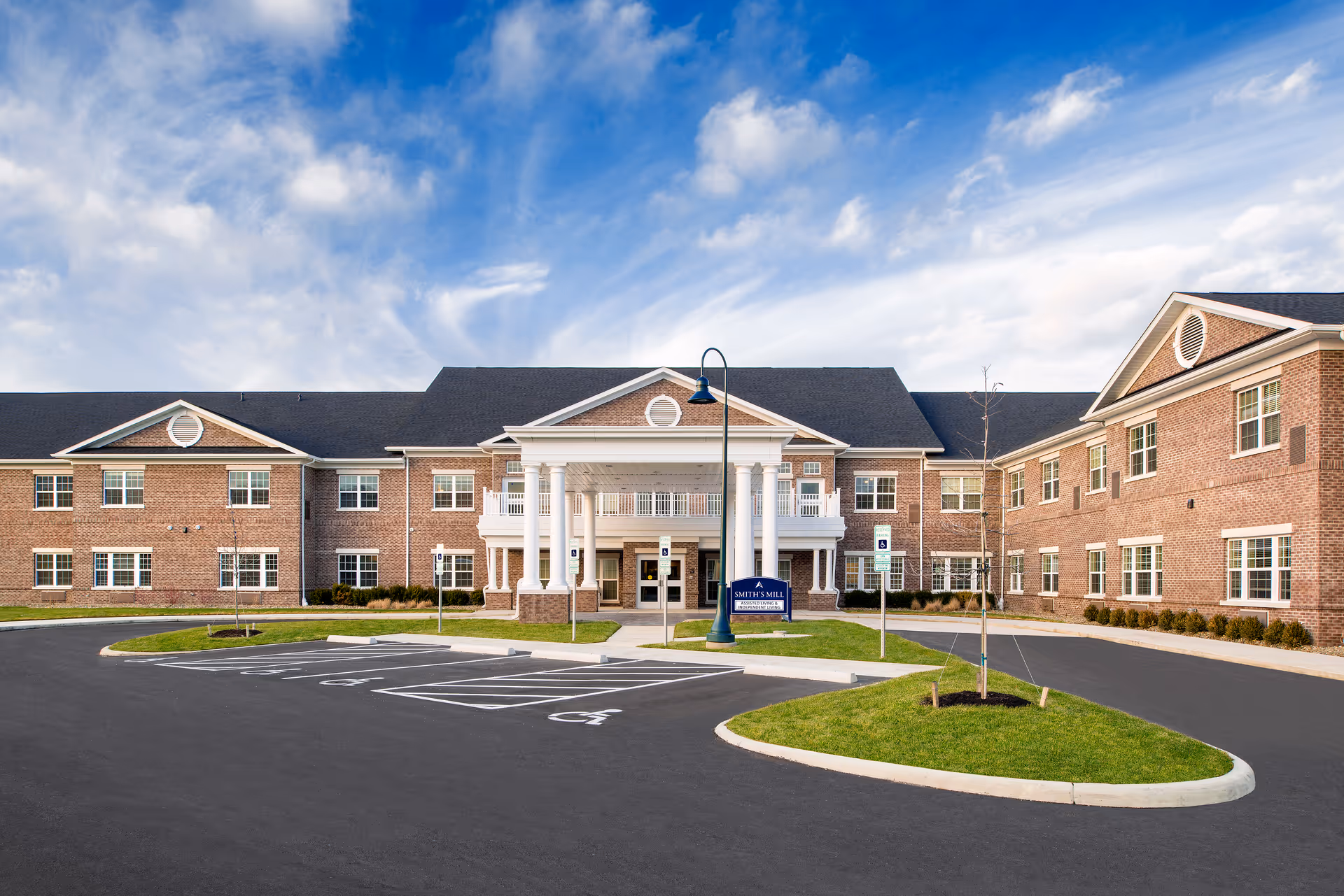 Brick senior living campus with a central entrance and accessible parking in sunny weather.