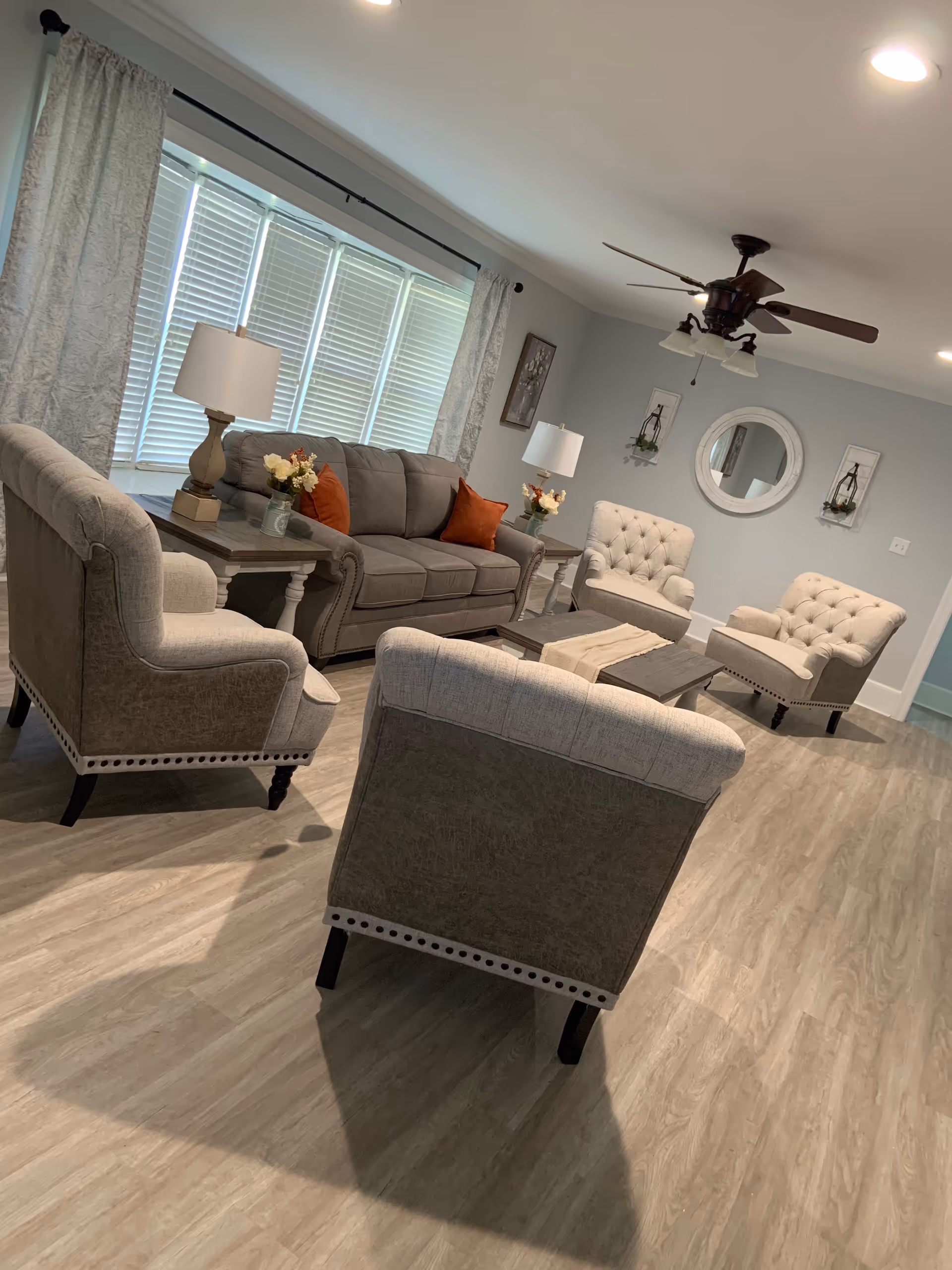 Cozy senior living living room with beige upholstered seating, lamps, and large windowed wall.