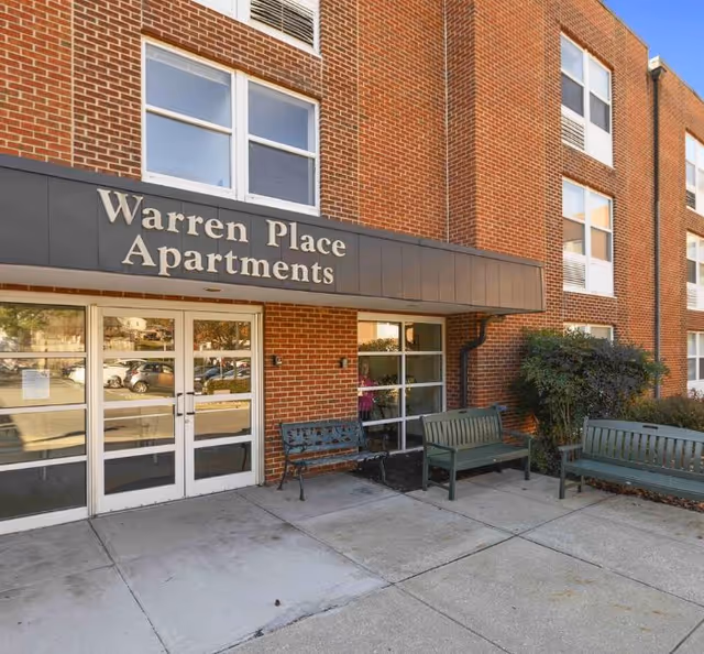 Brick exterior of a senior apartment building with Warren Place Apartments sign and outdoor benches.