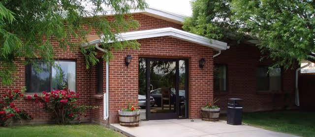 Brick exterior nursing facility entrance with glass doors and surrounding planters