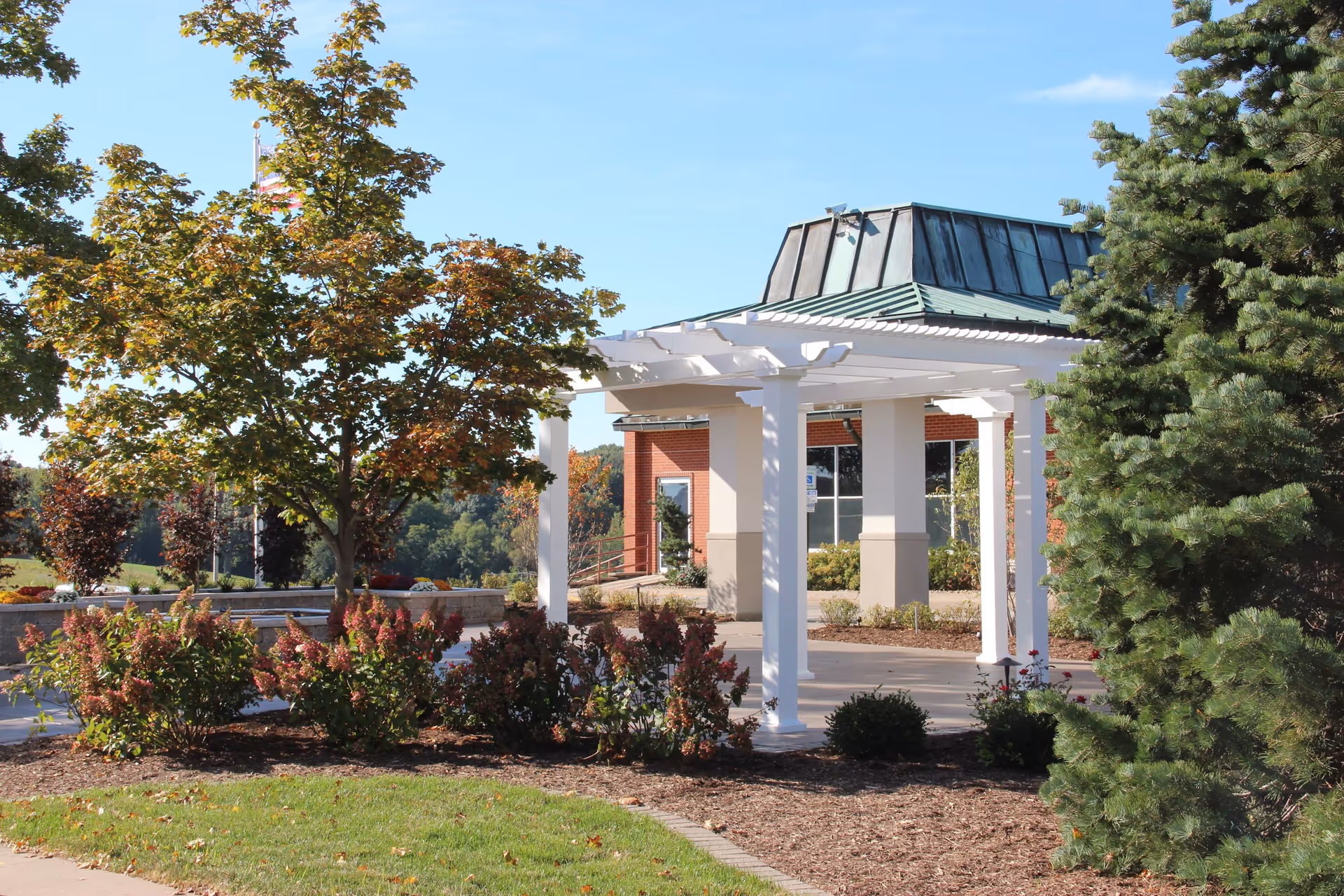 Exterior view of The Alverno Senior Care Community with a white pergola, trees, and landscaping.