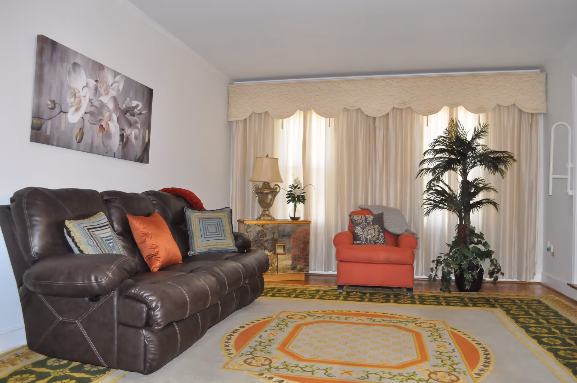 A cozy living room with brown leather sofa, red chair, and potted plants.