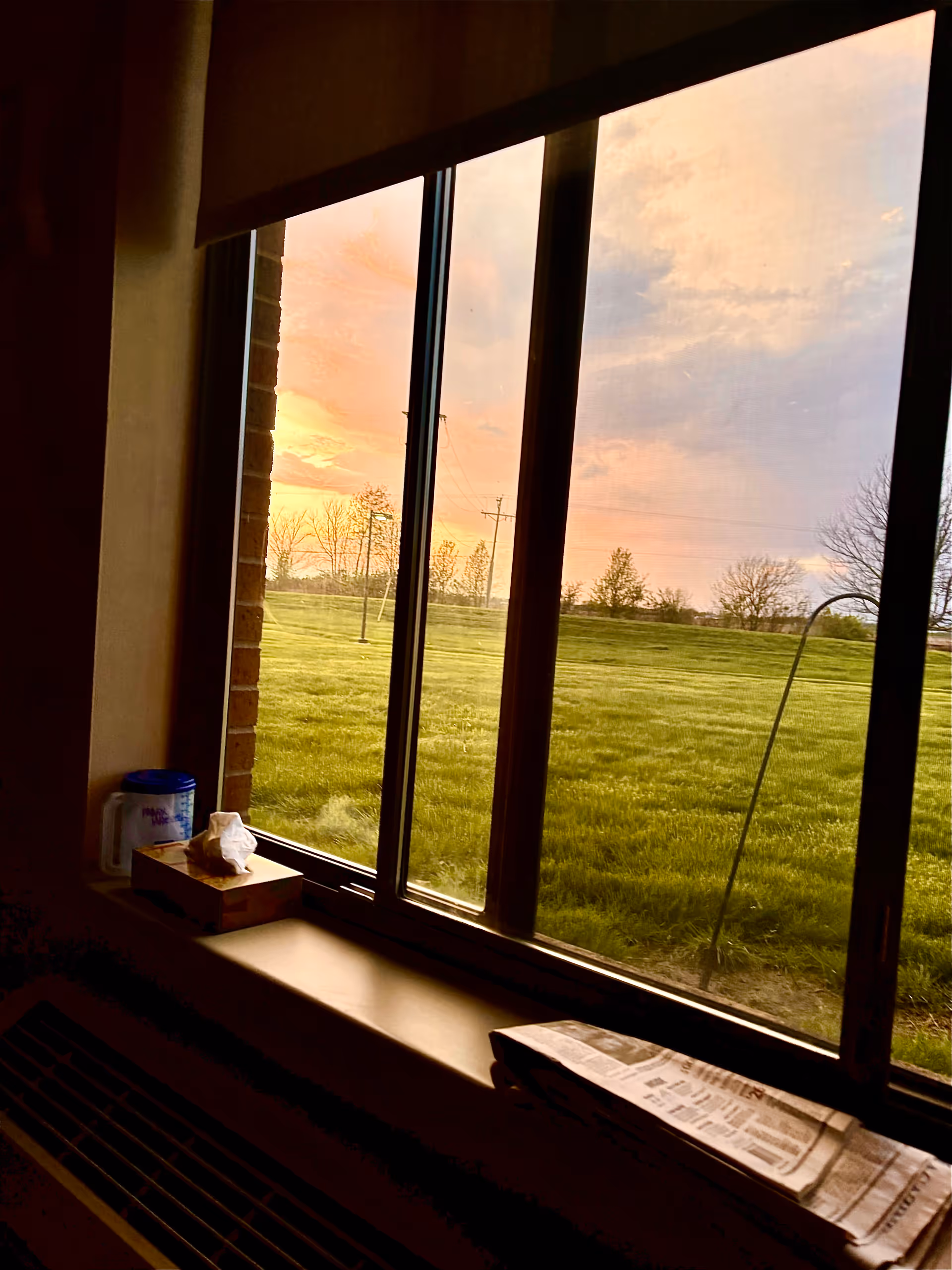Interior room with large window overlooking a grassy field at sunset.