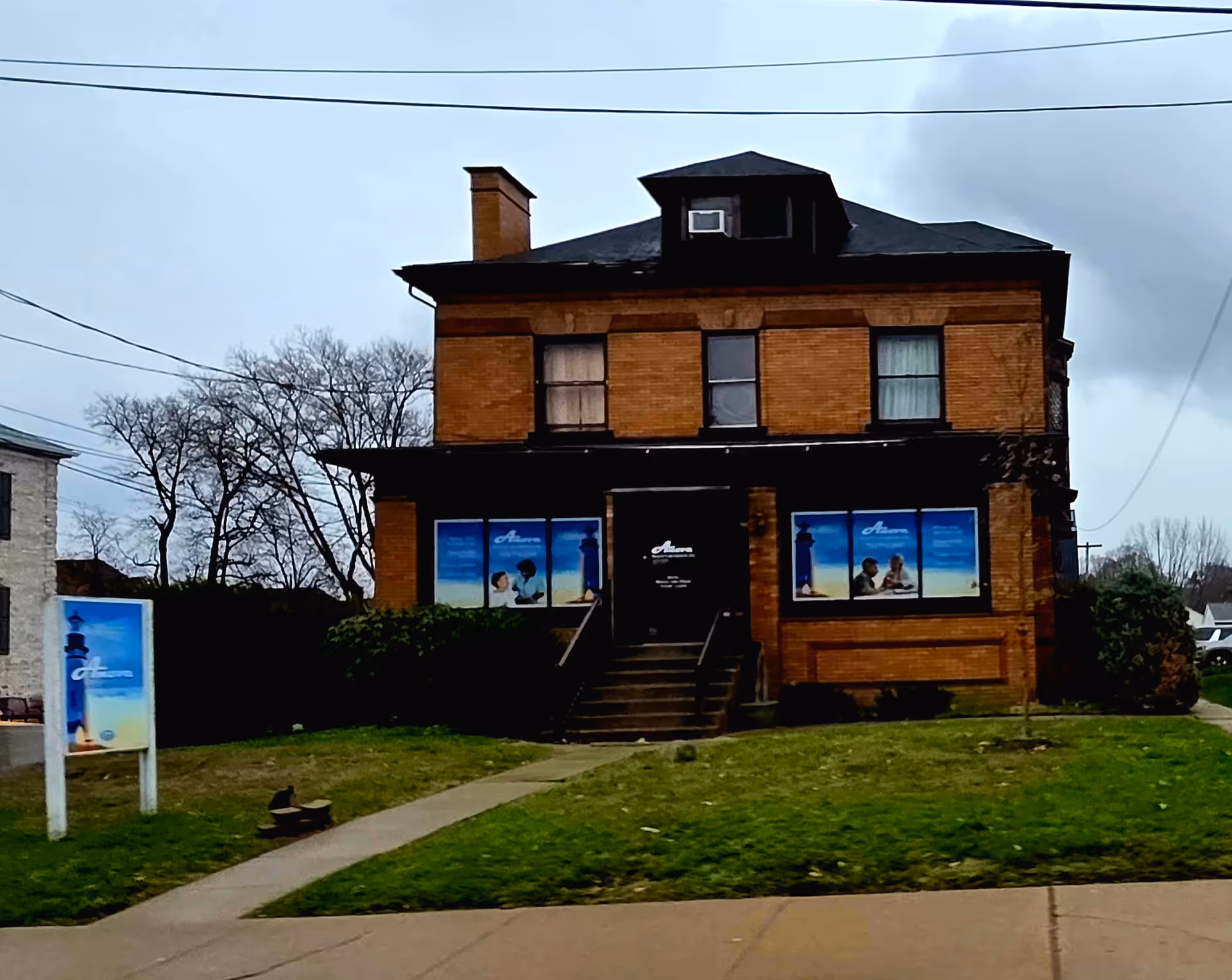 Brick two-story building with front stairs, large windows, and blue promotional posters.
