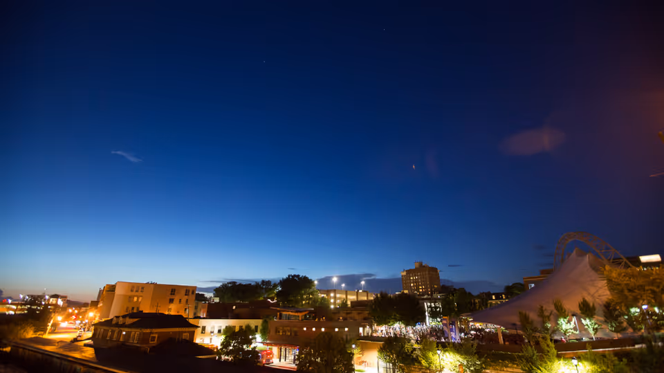 Nighttime view of a cityscape with buildings, trees, and a large illuminated tent.