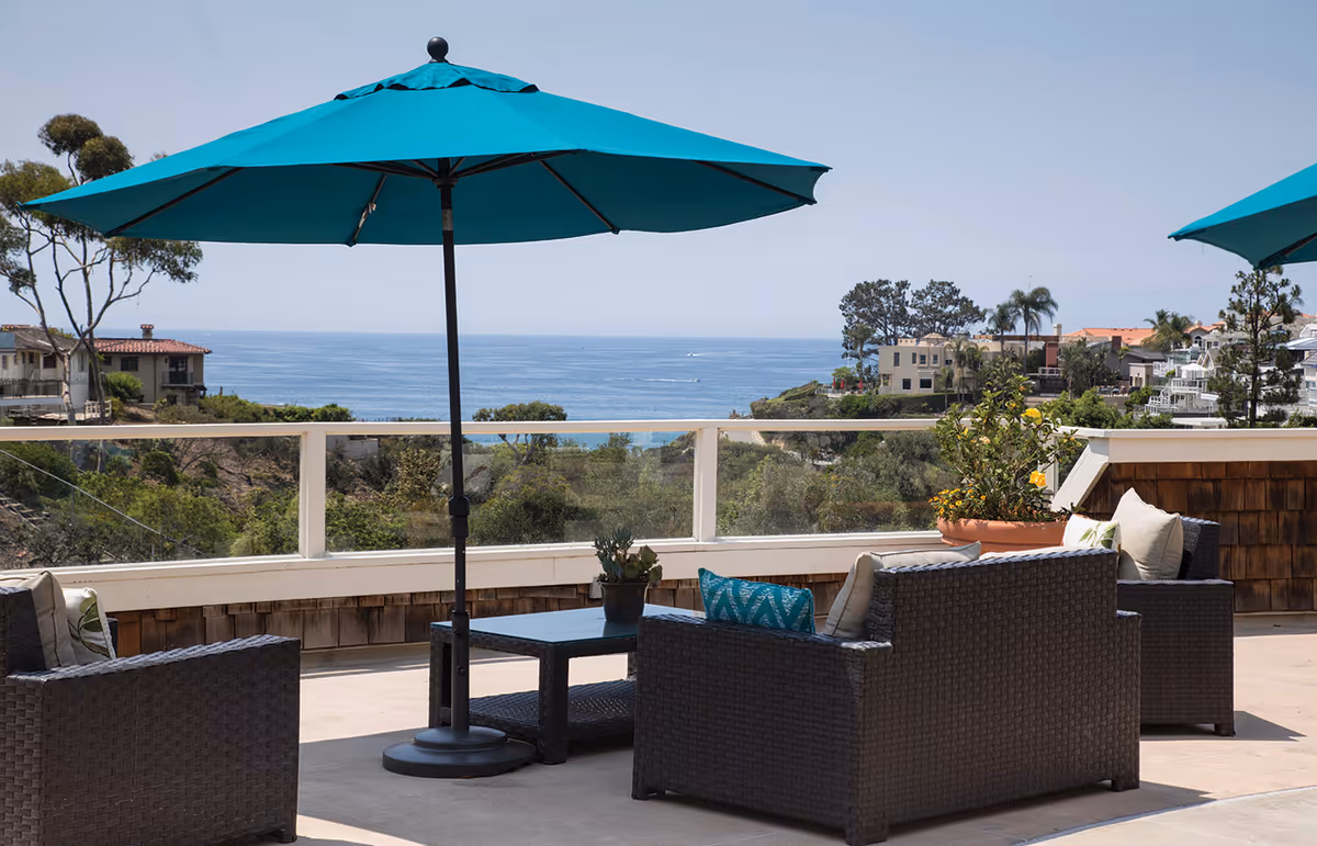 Outdoor terrace with wicker seating, turquoise umbrellas, and ocean view.