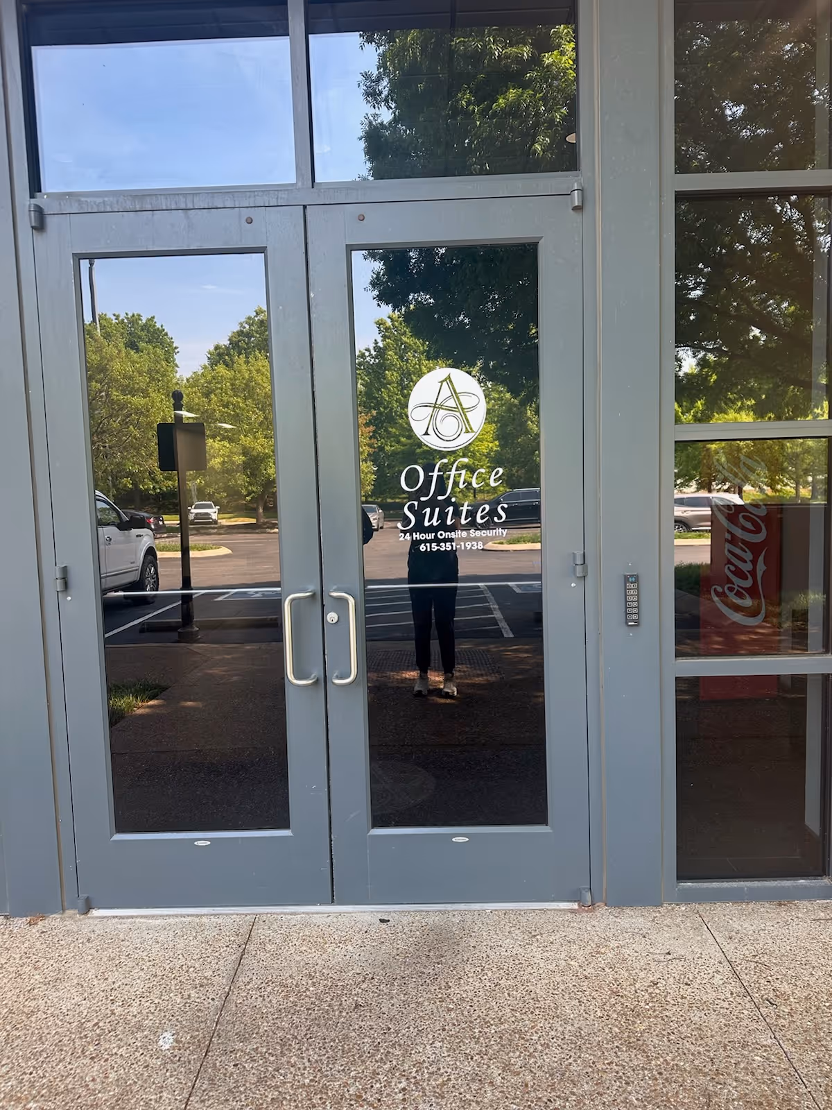 Glass doors with Office Suites logo reflect trees outside.