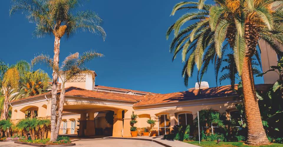 Sunny exterior view of The Village at Sherman Oaks with palm trees and arches.
