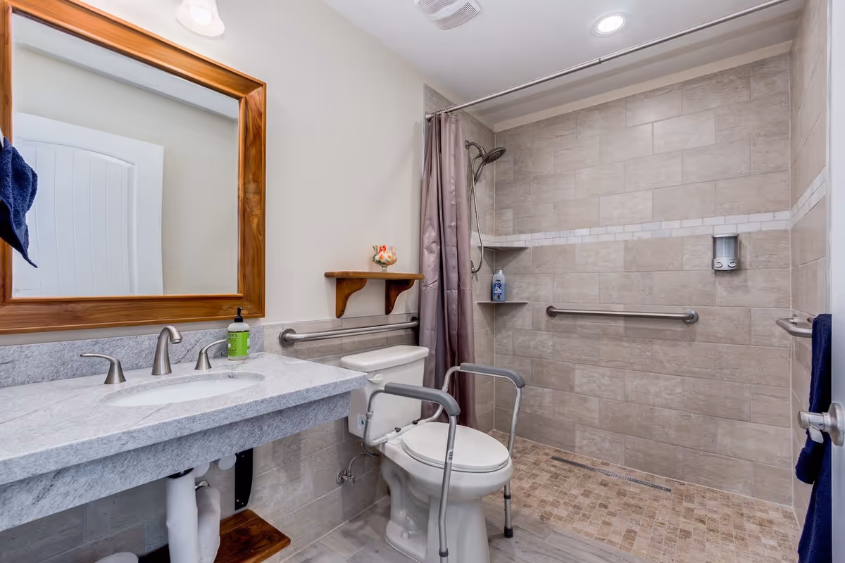 Accessible bathroom with sink, mirror, toilet, grab bars, and a walk-in shower.