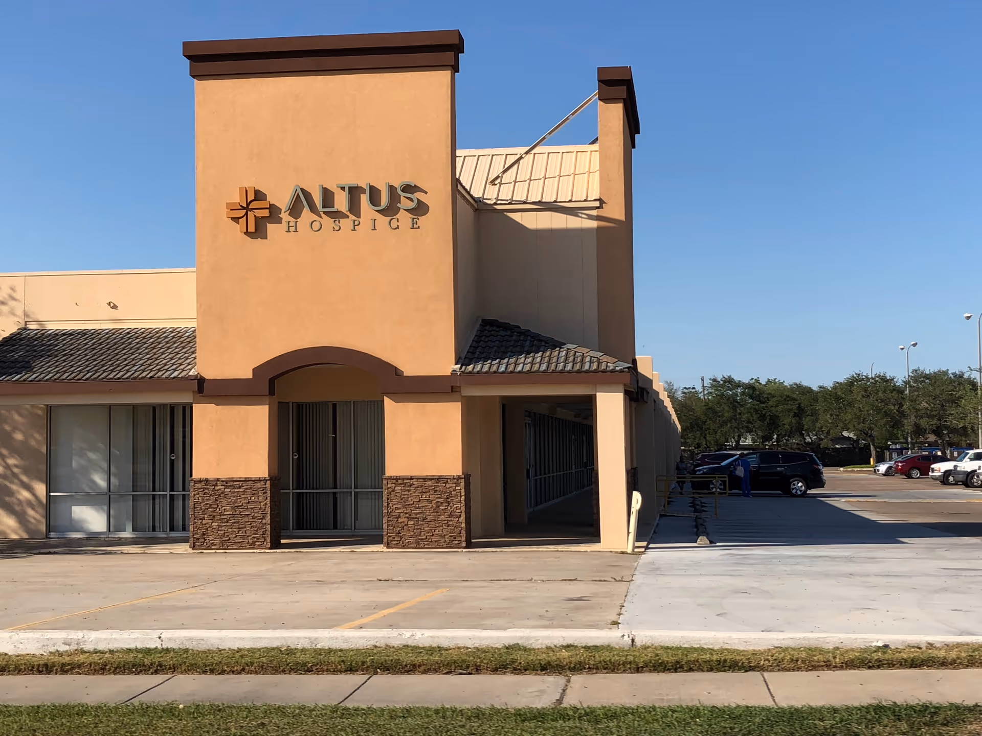 Tan Altus Hospice building with signage and surrounding parking lot under blue sky.