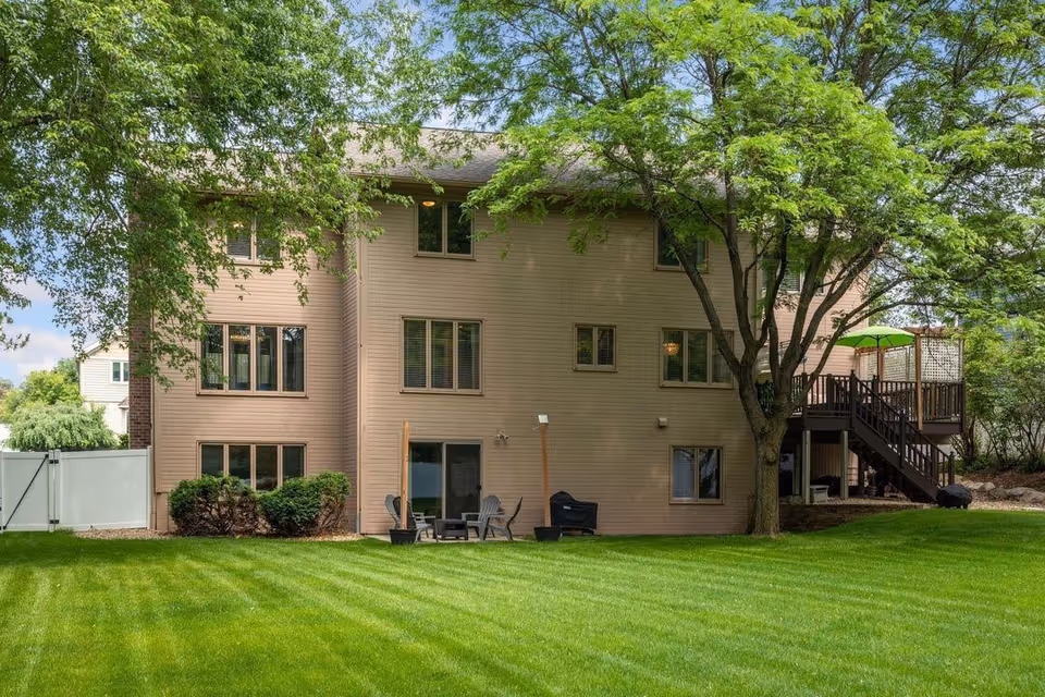 Two-story beige building with a deck, trees, and a manicured green lawn.