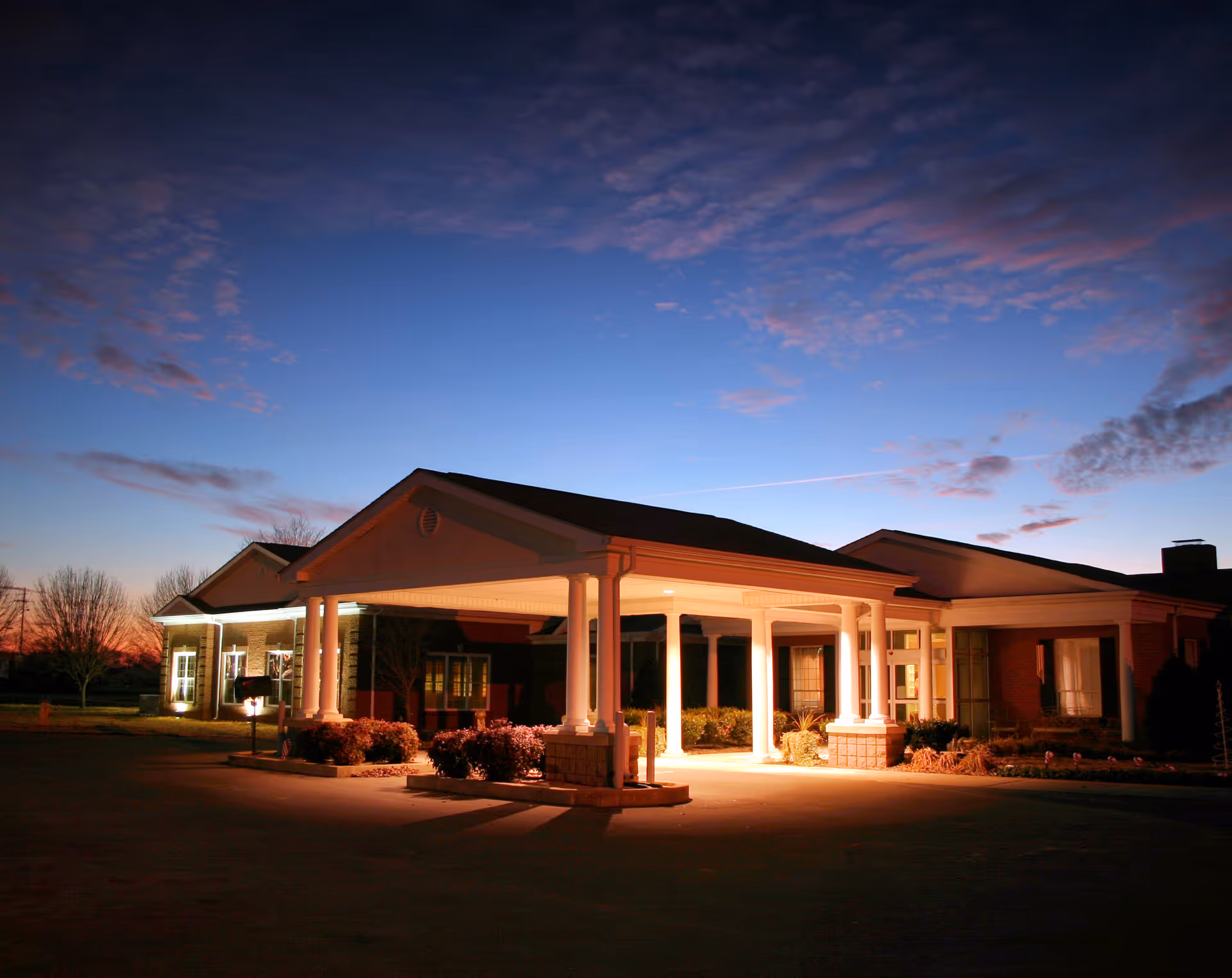 Exterior view of Stones River Manor entrance with illuminated portico at dusk.
