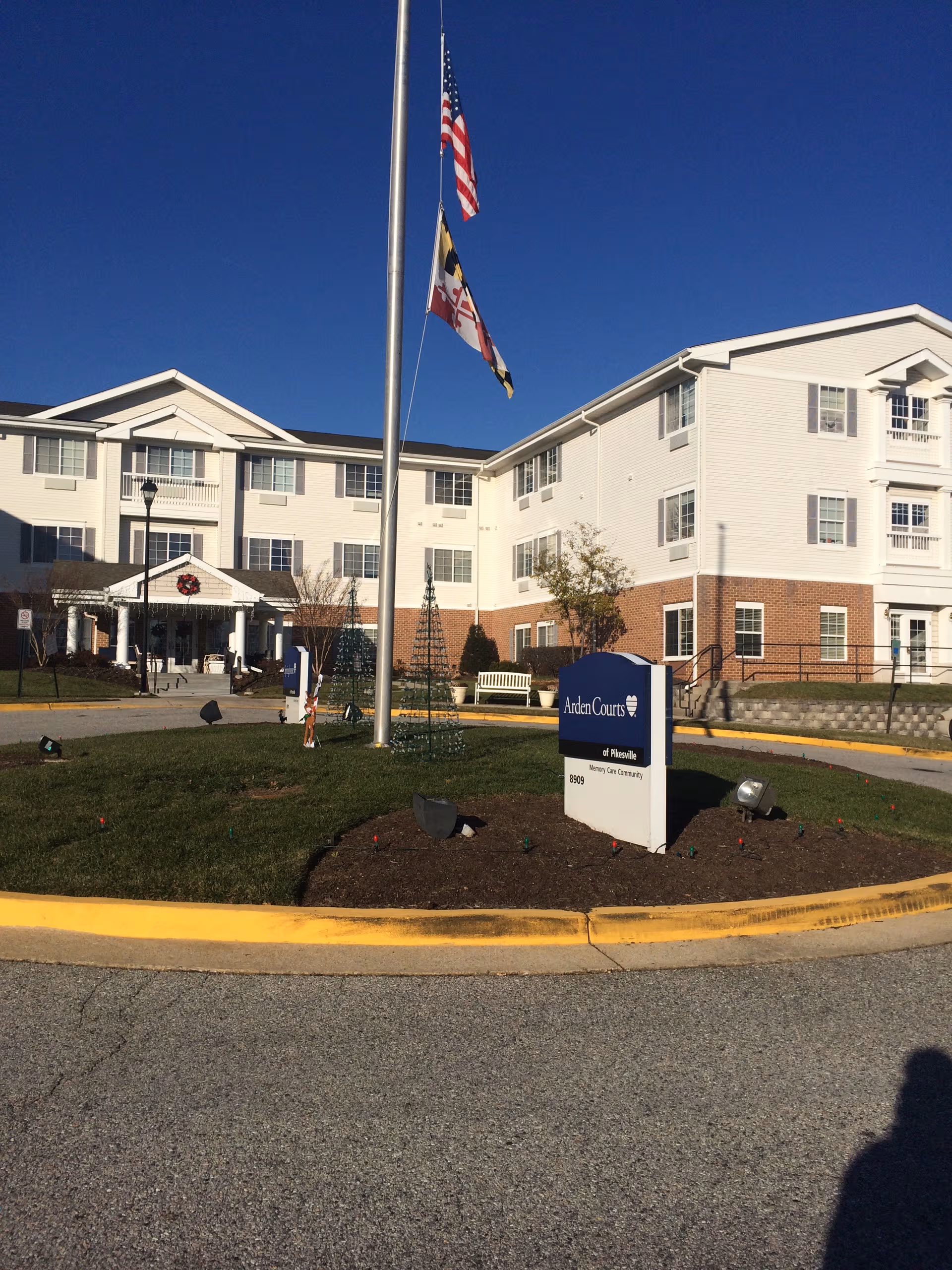 Three-story light-colored senior living building with flagpoles, entrance, and Arden Courts sign.