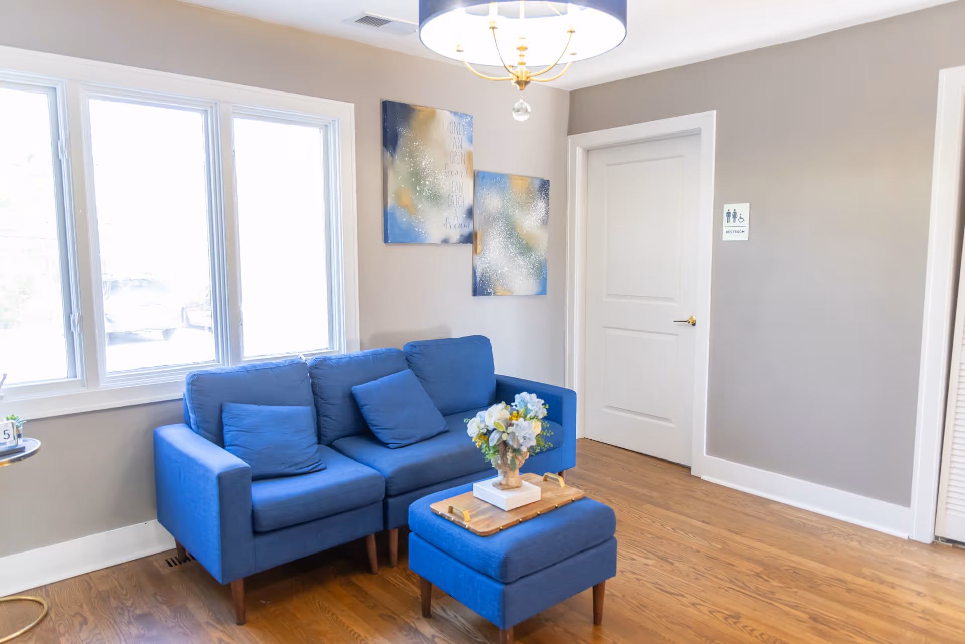 Blue sofa and ottoman in a modern lounge with artwork and large windows.