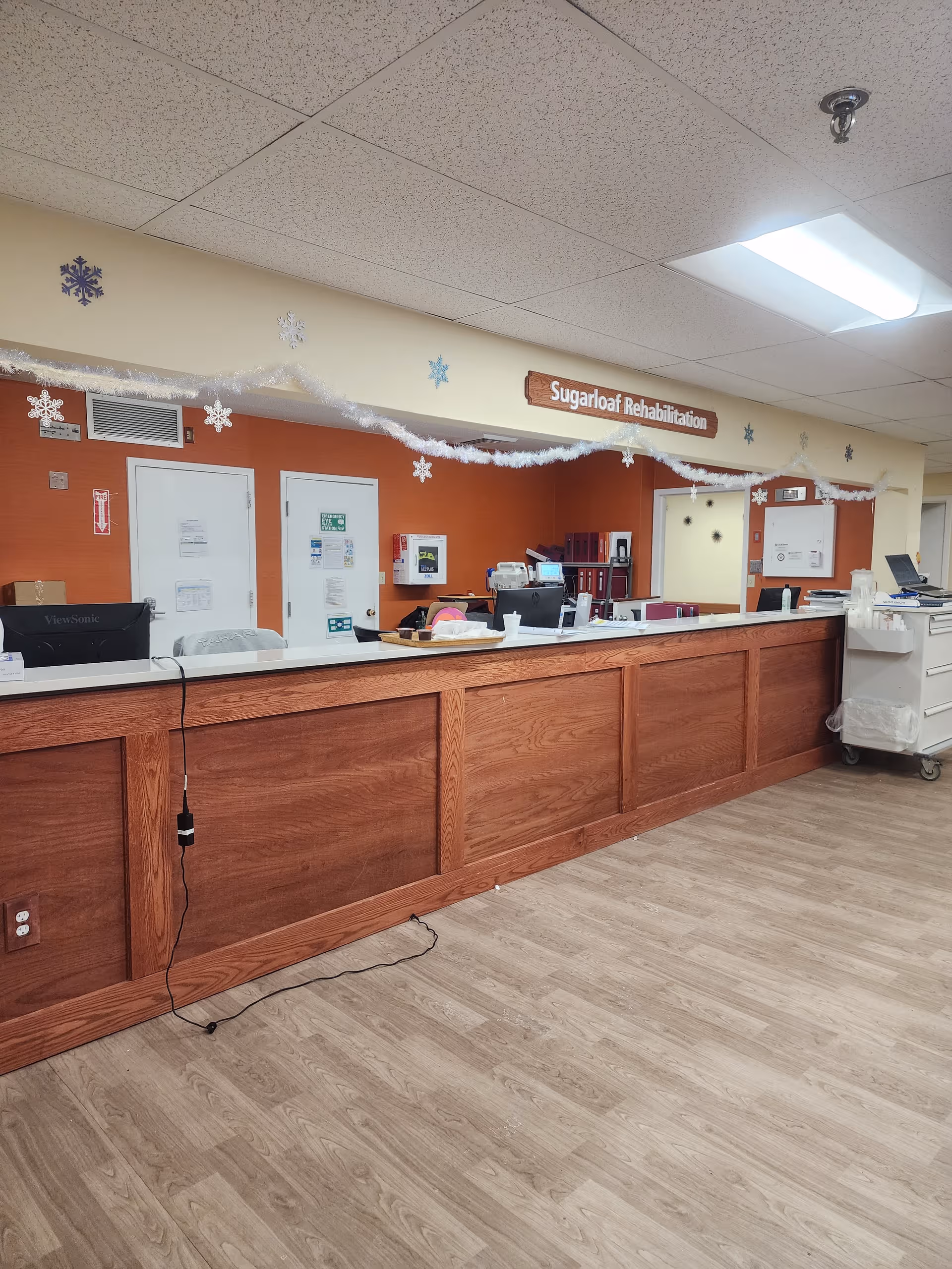 Indoor rehab facility lobby featuring a long wooden check-in desk and holiday decor.