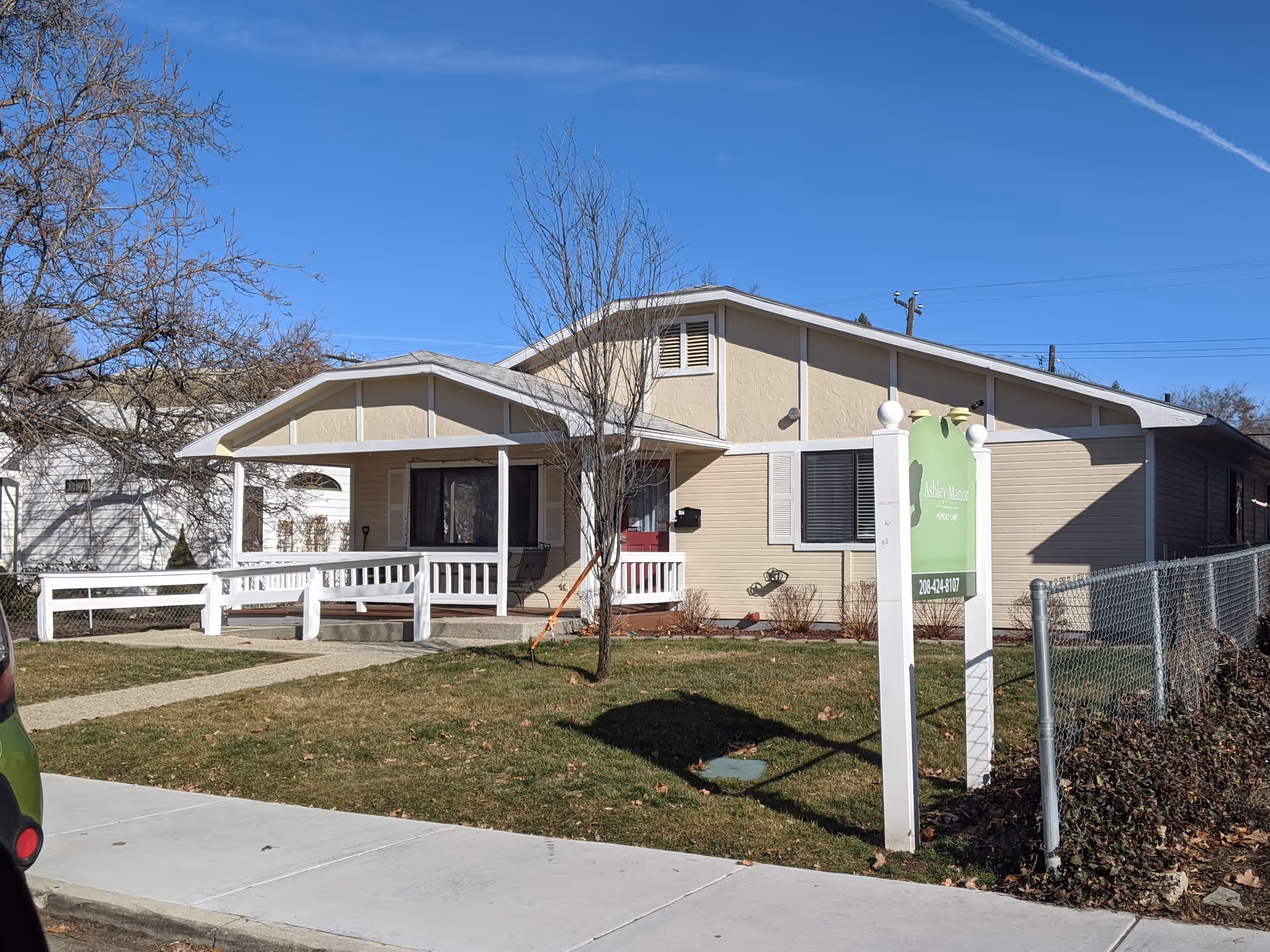Single-story beige memory care facility with white porch and green sign at front.