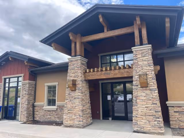 Front entrance of a modern building with stone pillars and wooden beams.