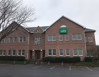 Brick two-story building with a green UDS sign and a front parking lot.