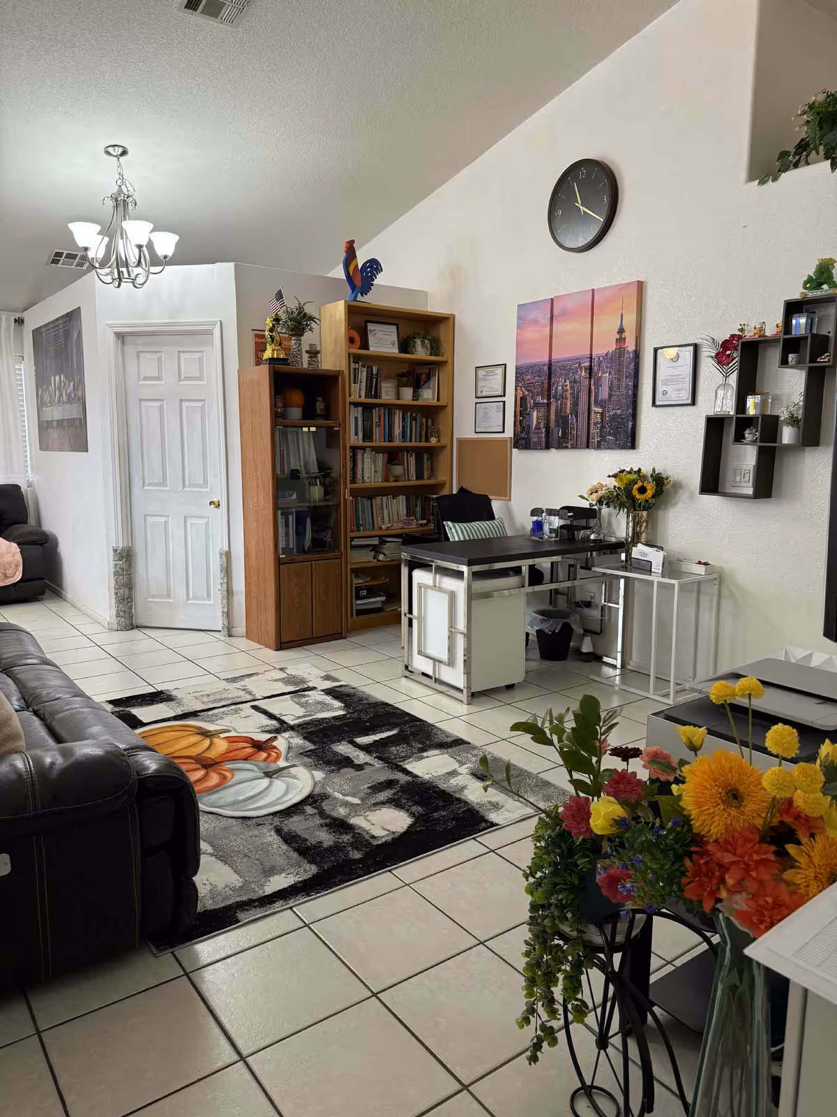 Cozy living room in a care home with sofa, bookshelves, desk, chandelier, and colorful flowers.