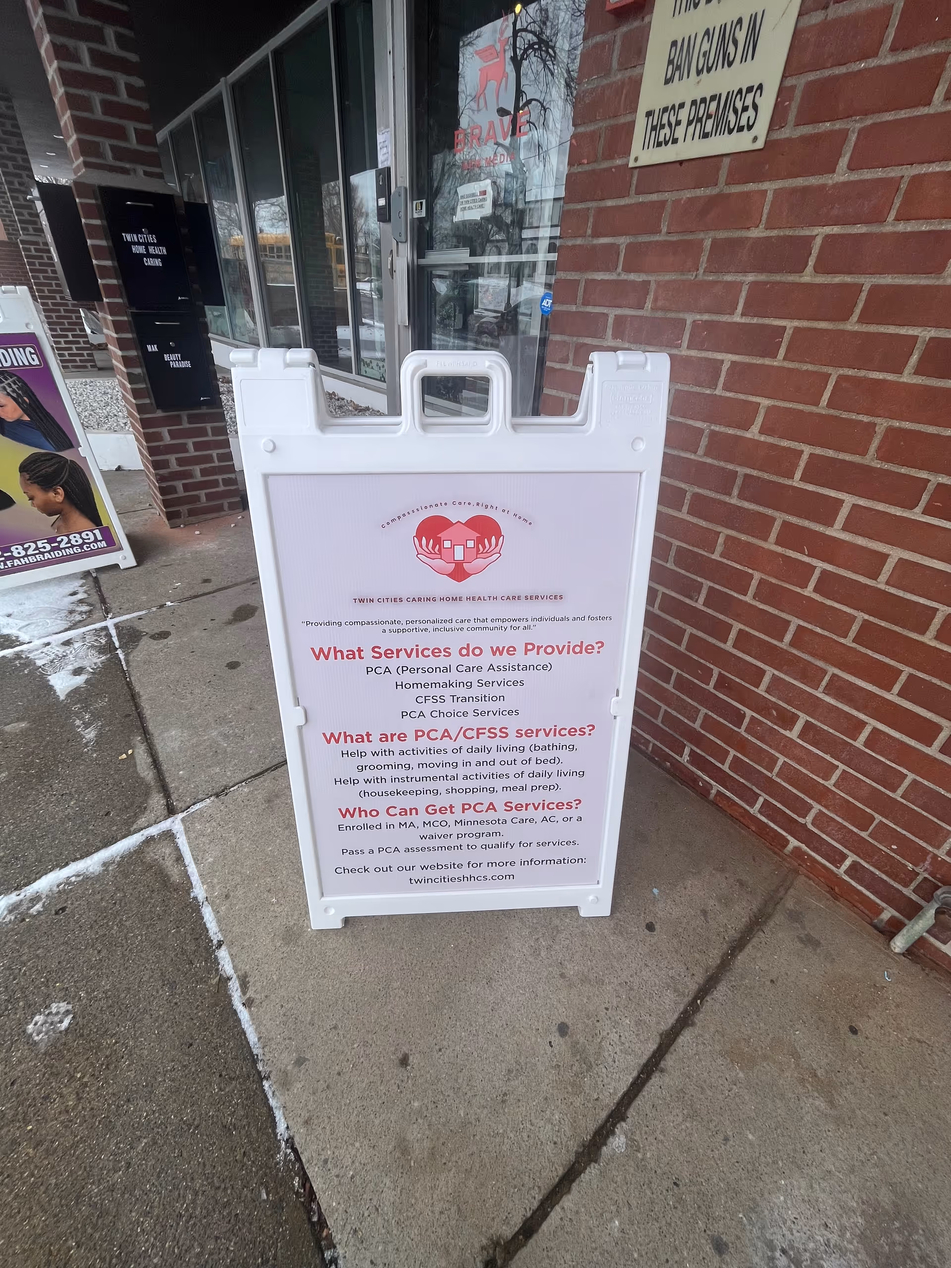 White sidewalk signboard advertising Twin Cities Caring Home Health Care Services outside a brick storefront.