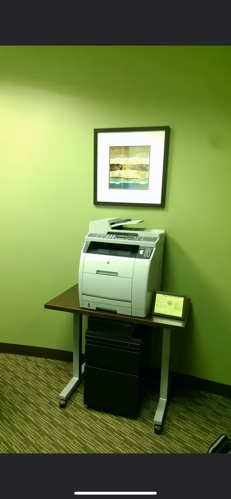 Printer on a small table against a green wall with framed artwork.