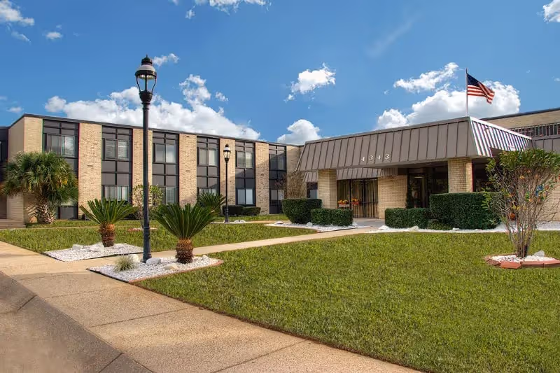 Exterior view of Bayside Health and Rehabilitation Center with front entrance, lawn, and flag.