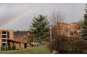 Rainbow arches over The Community at Rockhill campus with brick buildings and trees.