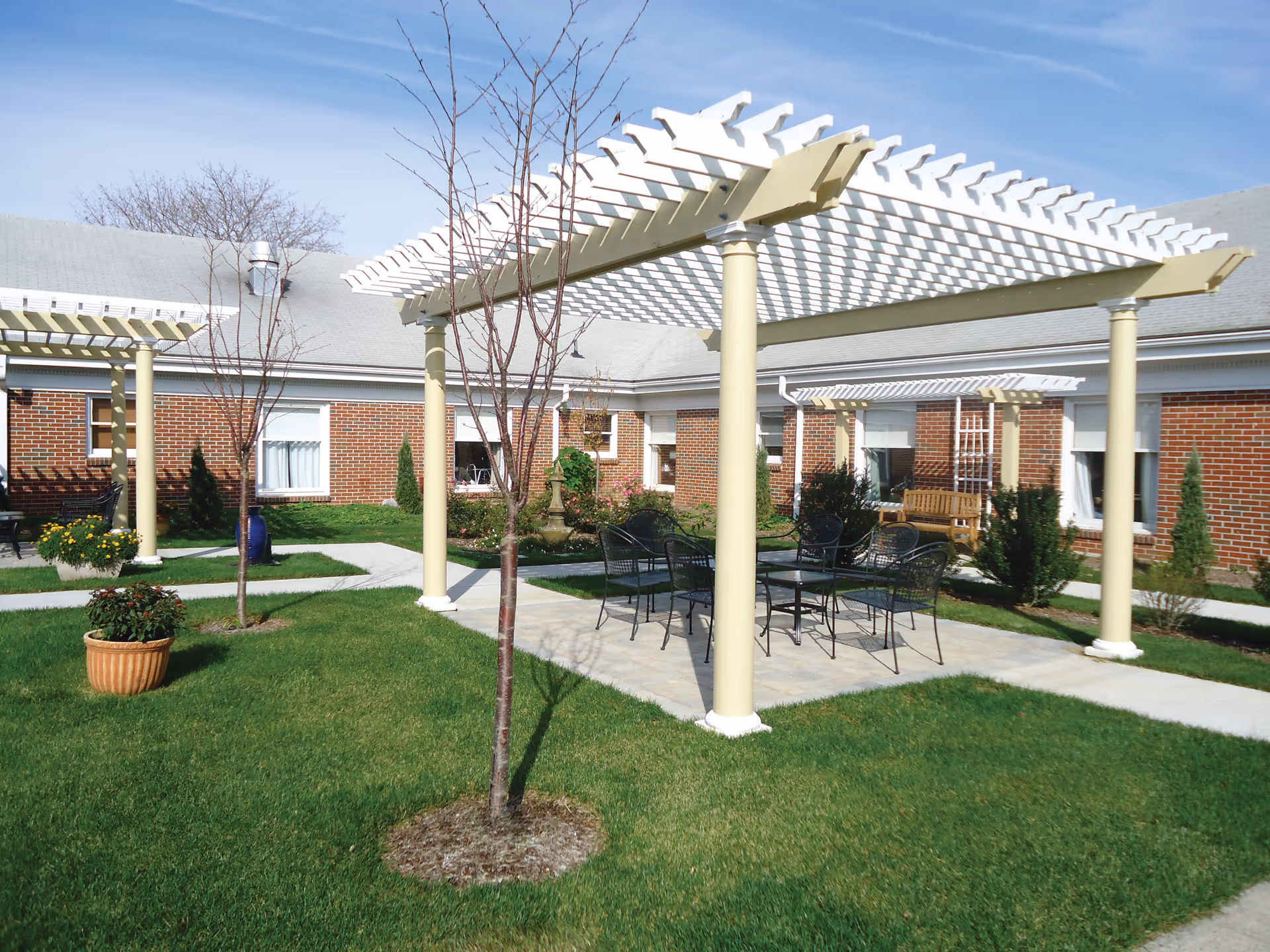 Brick building courtyard with white pergolas, a paved patio, and metal outdoor tables.