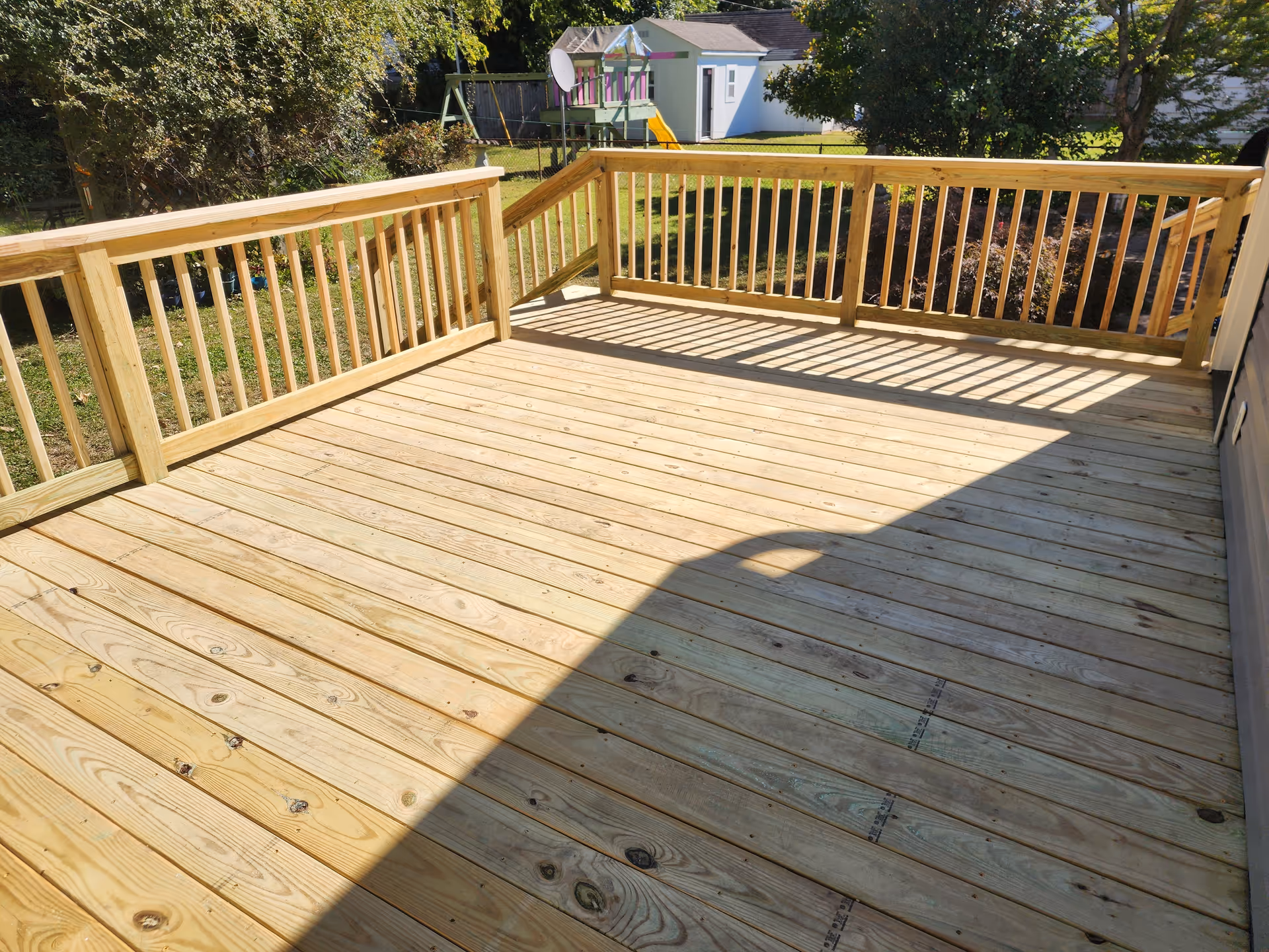 Wooden outdoor deck with railing overlooking a yard and distant playground.