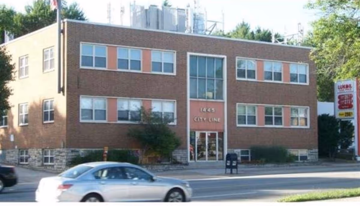 Brick three-story building with a glass central entrance and cars parked outside