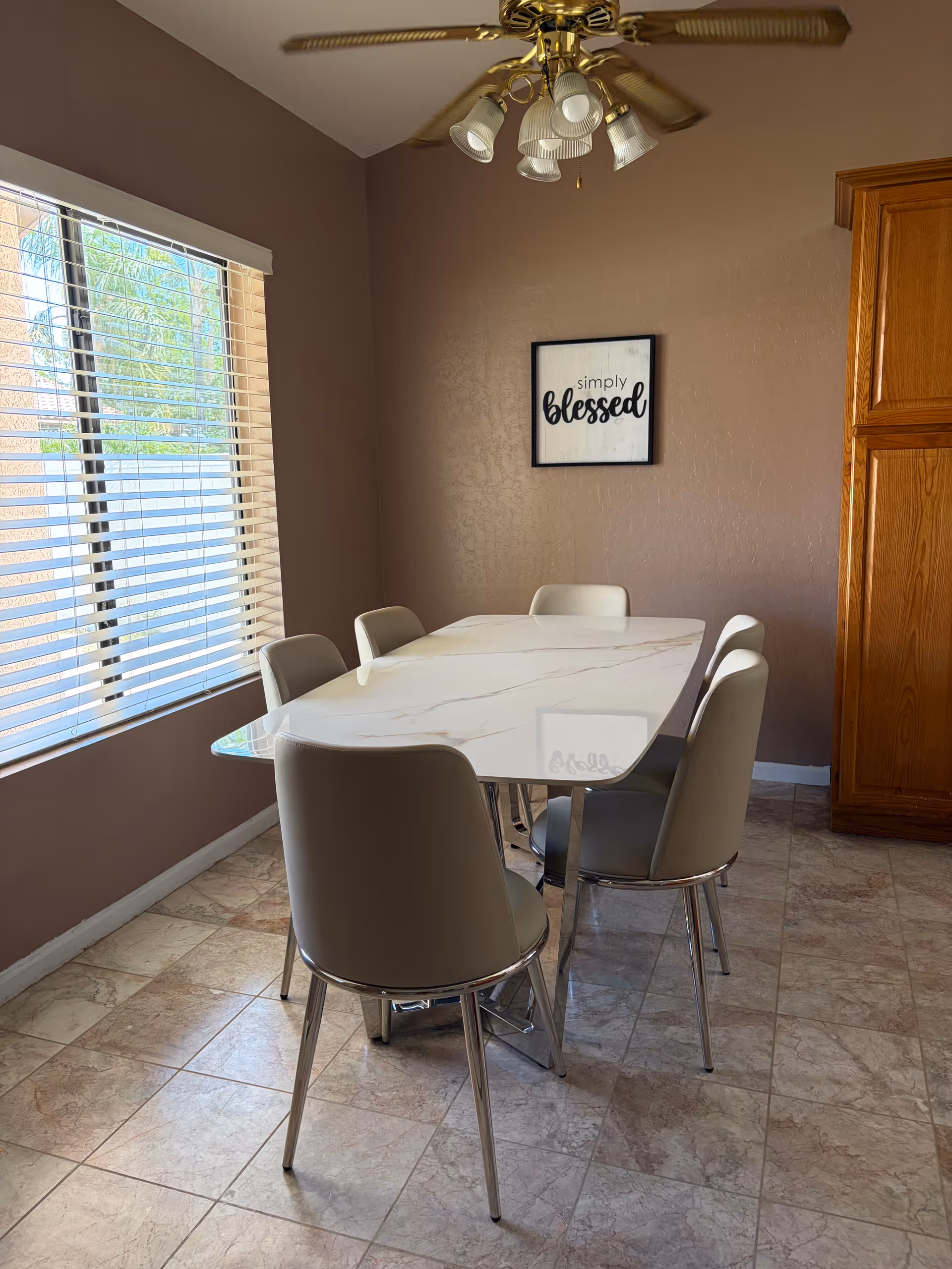 A dining room setup with a marble table, beige chairs, window, and wall art.