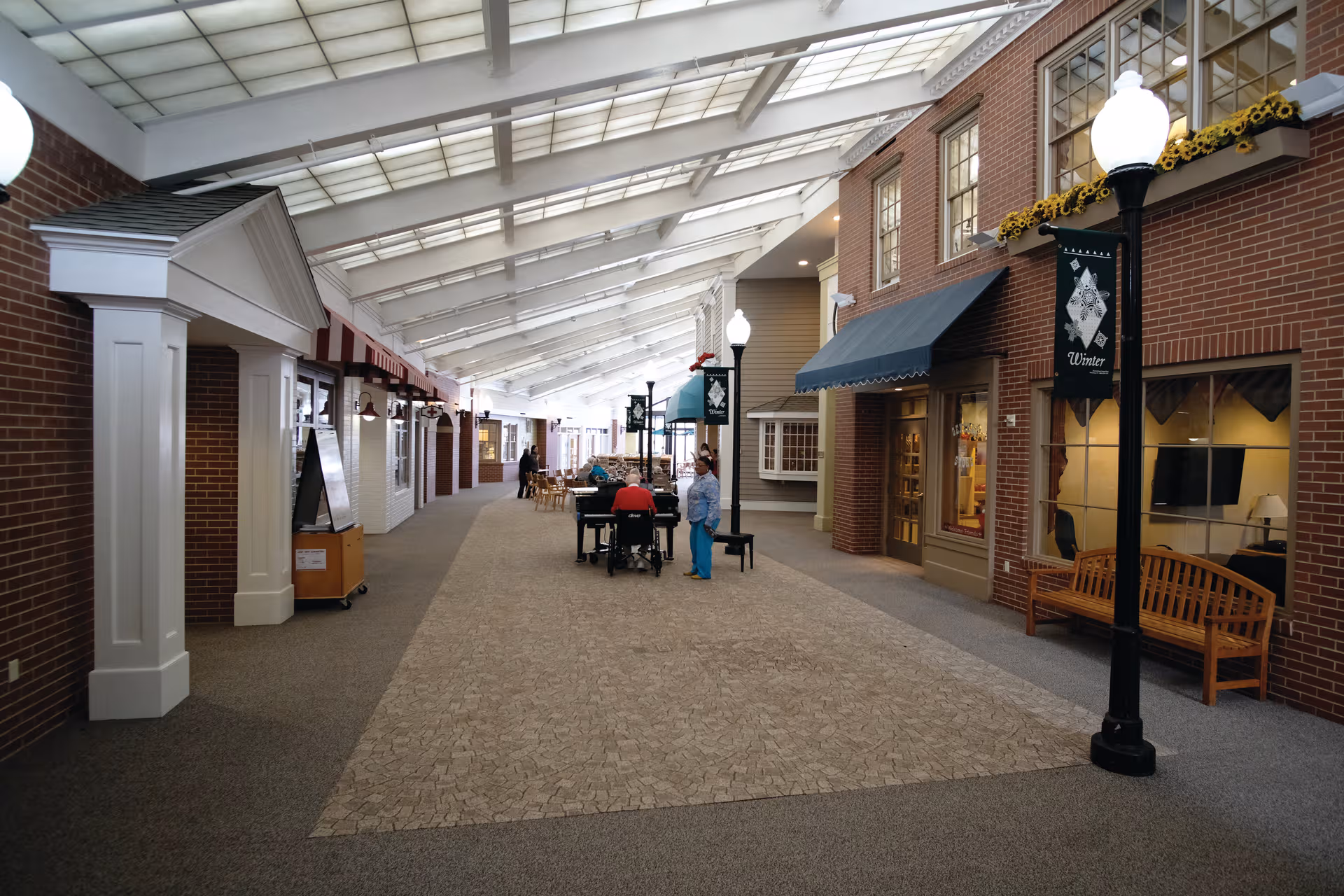 Indoor mall-style corridor with brick storefronts, benches, and skylight ceiling.